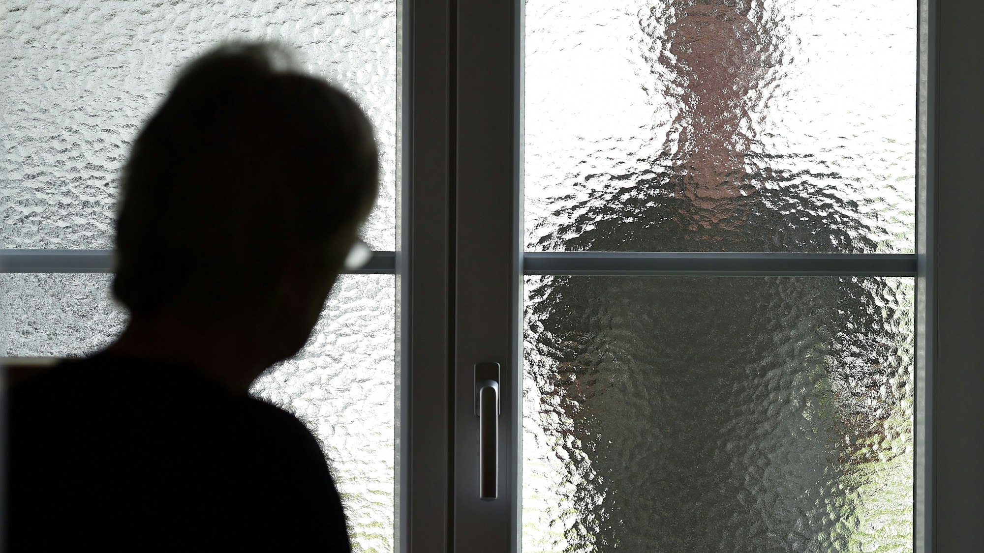 Eine Frau steht an einer Glasscheibe, hinter der ein Stalker steht. (gestellte Szene).