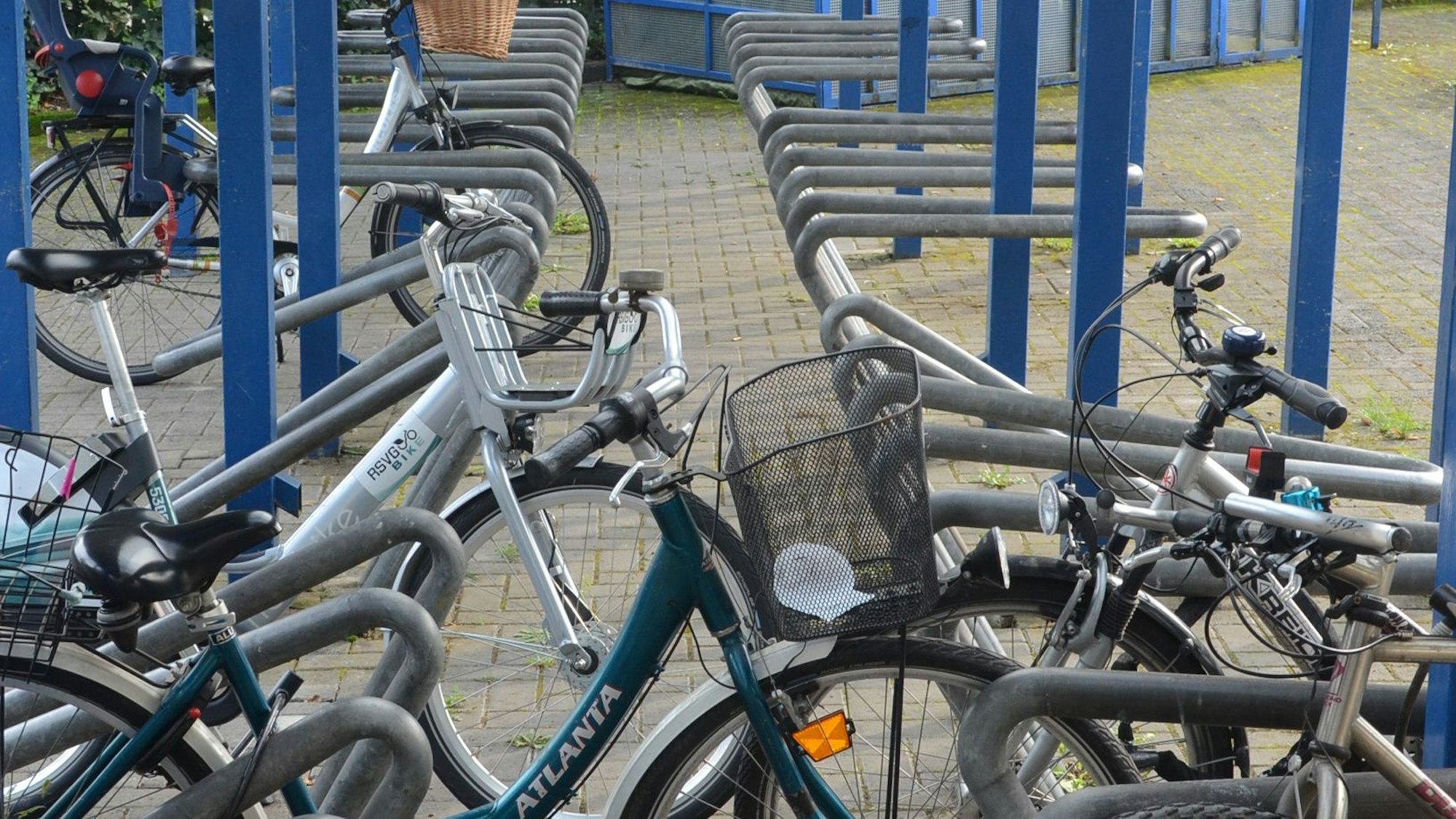 Fahrräder sind an Ständer aus grauem Metallrohr angelehnt. Blaue Pfosten tragen das Dach.
