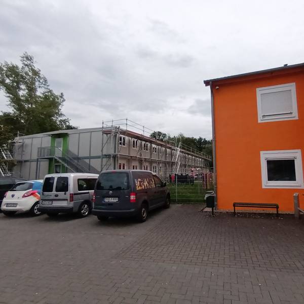 Eingerüstete Container neben einem Wohn- und Bürogebäude.
