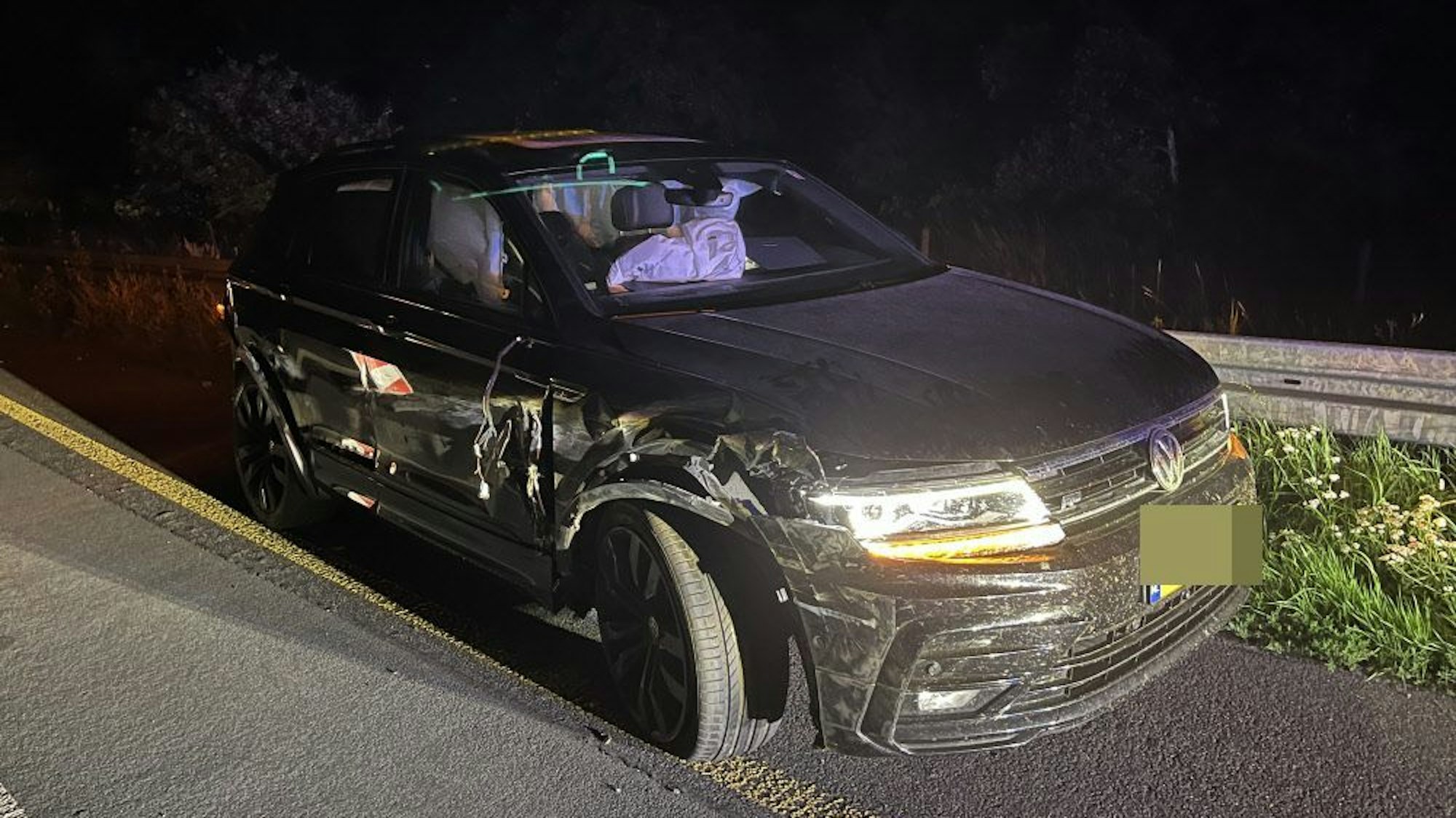 Ein dunkles Auto mit holländischem Kennzeichen steht beschädigt auf dem Standstreifen. Alle Airbags haben ausgelöst und füllen den Innenraum des Wagens.
