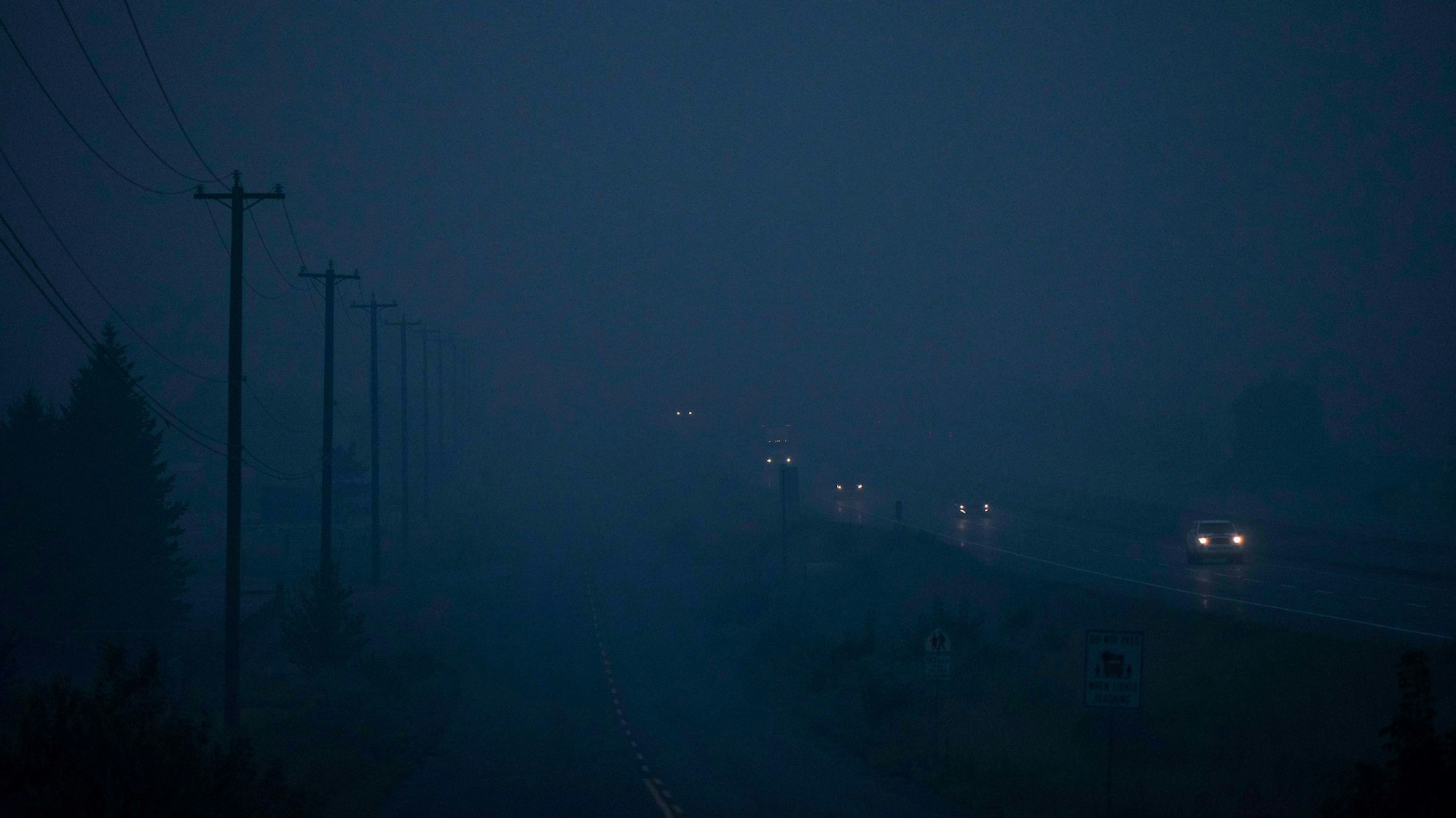 Autos fahren über eine vom Rauch vernebelte Straße, am linken Bildrand sind Silhouetten von Leitungsmasten zu erkennen.