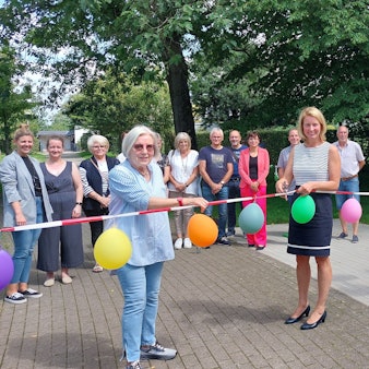 Zwei Frauen schneiden ein Absperrband, geschmückt mit Luftballons durch. Dieses ist an Outdoorfitnessgeräten befestigt.