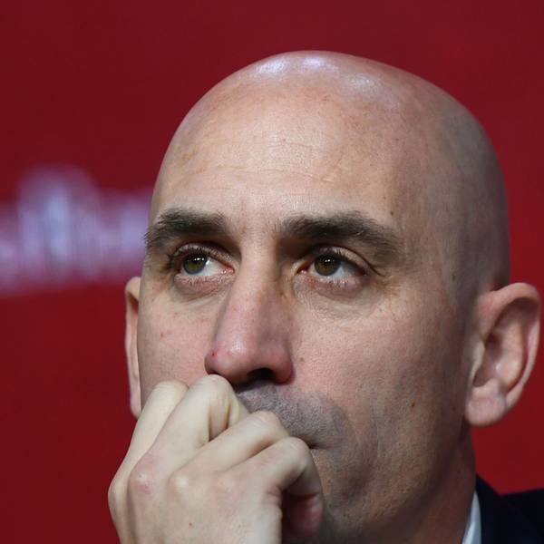 Nahaufnahme von Luis Rubiales Gesicht vor einem unscharfen roten Hintergrund - Rubiales hält eine Hand am Mund und schaut in die Ferne.