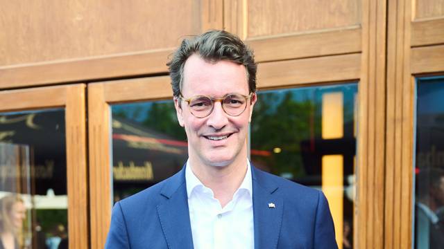 Hendrik Wüst (CDU), Ministerpräsident des Landes Nordrhein-Westfalen, lächelt vor Glasscheiben mit hölzernem Rahmen.