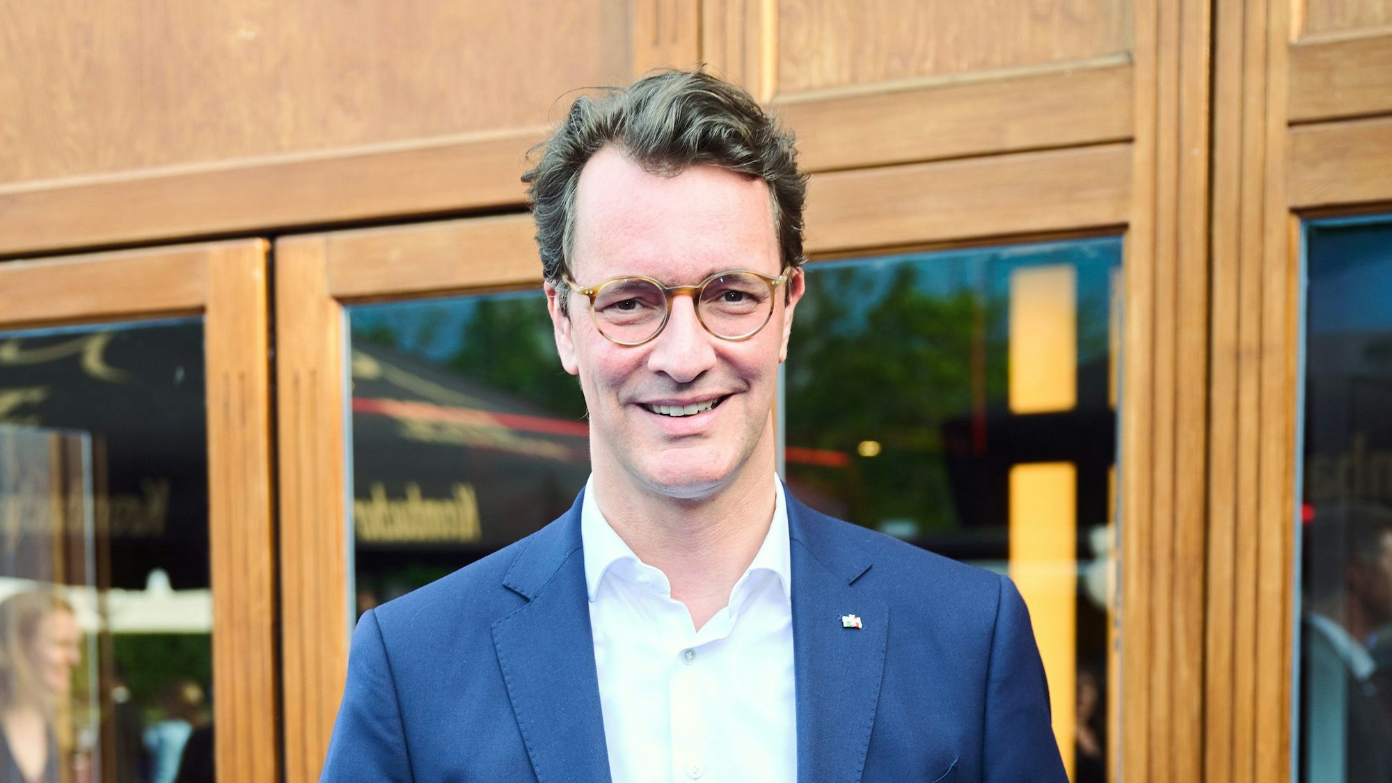 Hendrik Wüst (CDU), Ministerpräsident des Landes Nordrhein-Westfalen, lächelt vor Glasscheiben mit hölzernem Rahmen.