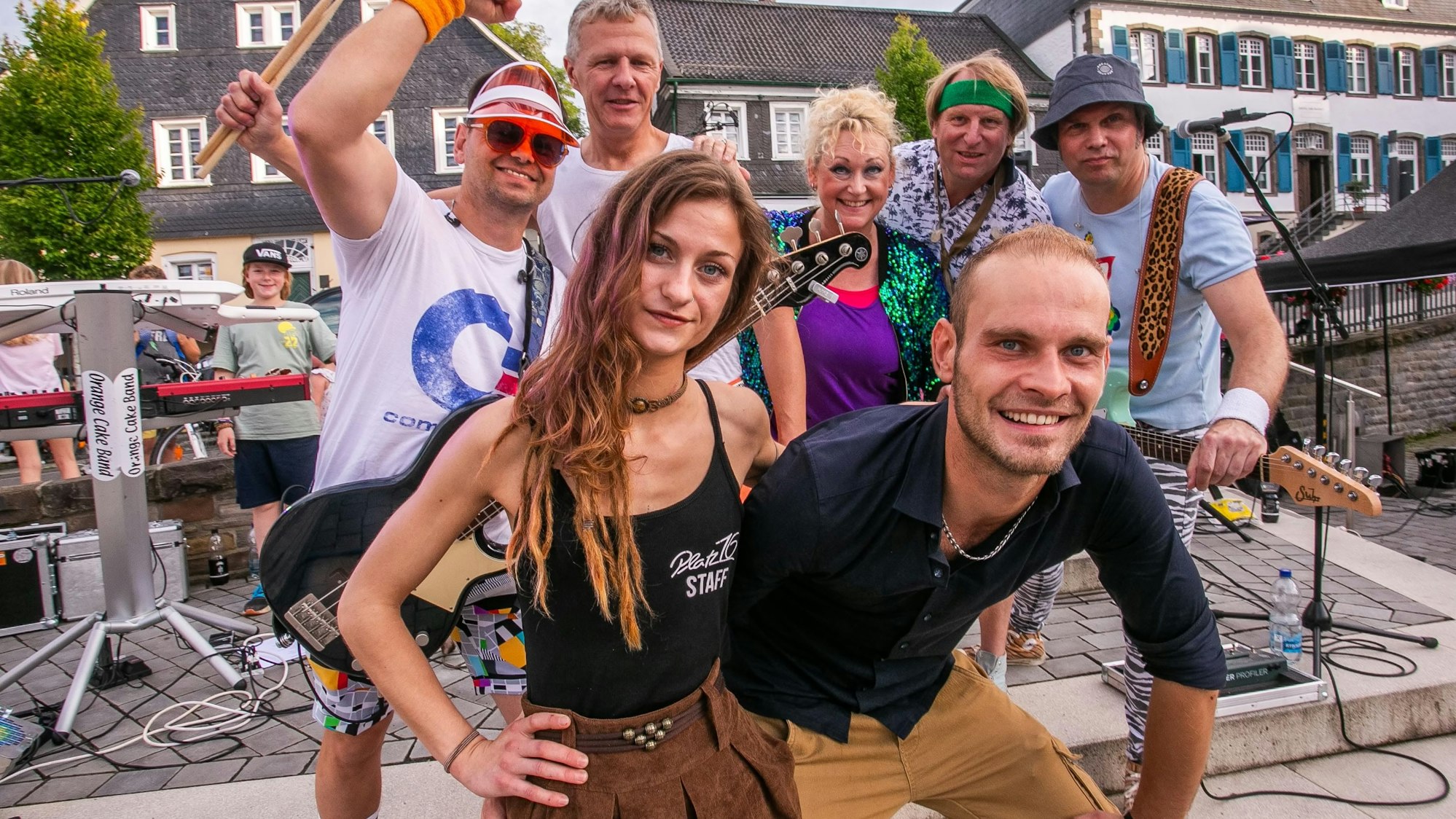 Im Bild eine Frau und ein Mann vor einer fünfköpfigen Band, die im Stile der 80er-Jahre gekleidet ist.