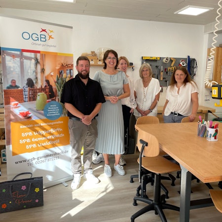 Eine Gruppe von Menschen steht lächelnd hinter einem Basteltisch.