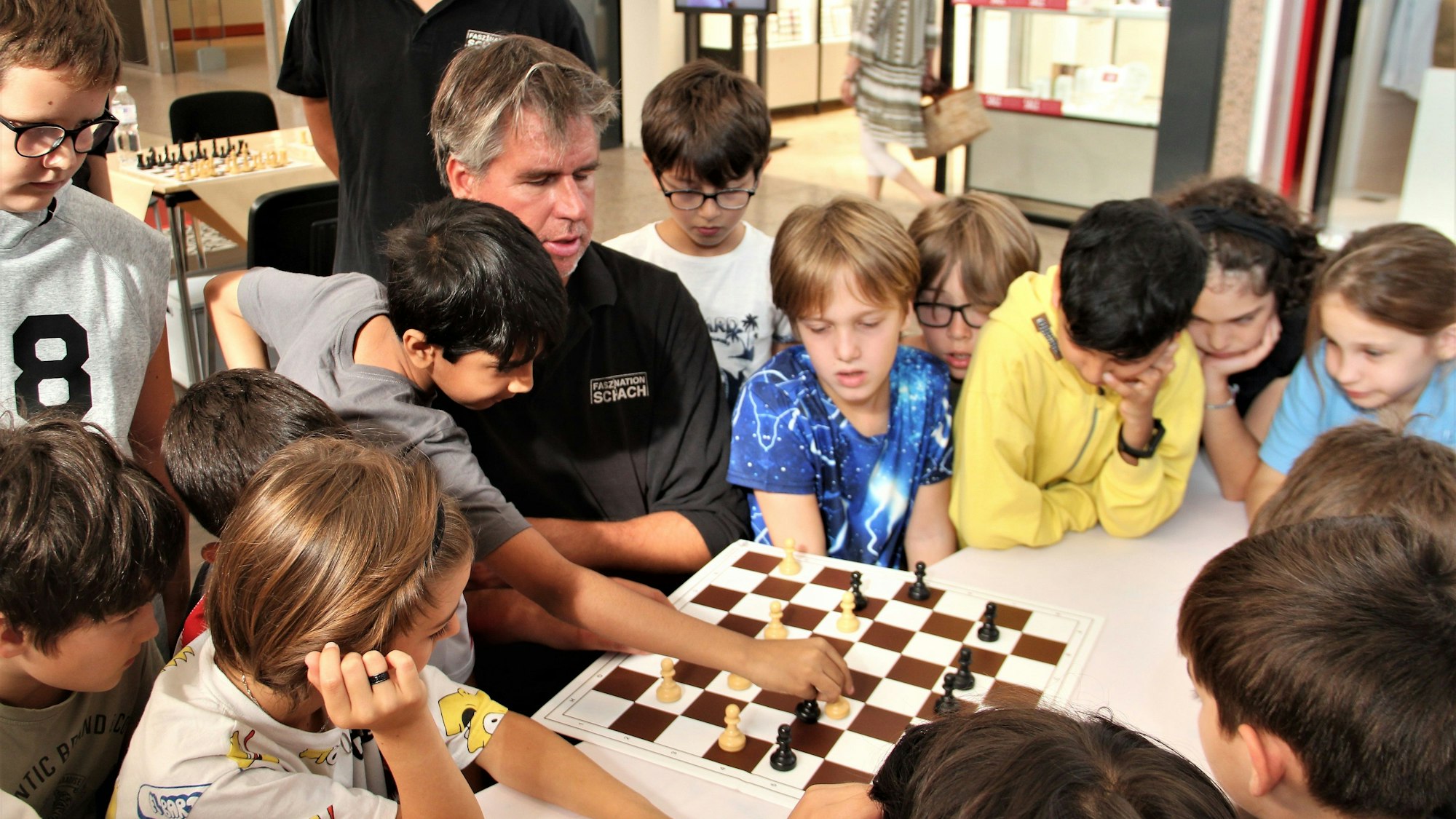 Der Profi Sebastian Siebrecht spielt Schach, um ihn herum stehen viele Kinder.