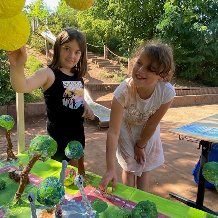 Zwei Mädchen sind über ein Pappmaché-Modell gebeugt. Ein Mädchen greift nach oben, eines nach unten.