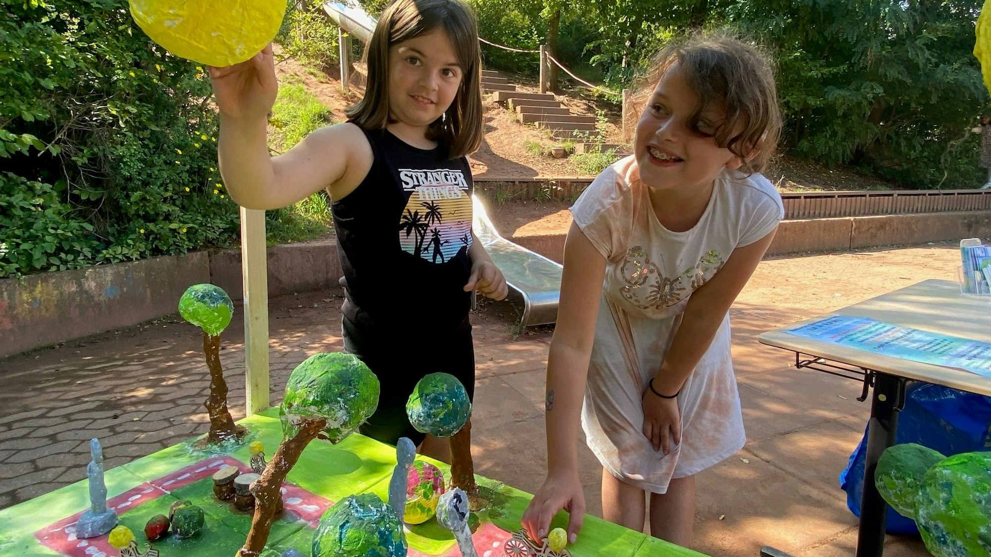 Zwei Mädchen sind über ein Pappmaché-Modell gebeugt. Ein Mädchen greift nach oben, eines nach unten.