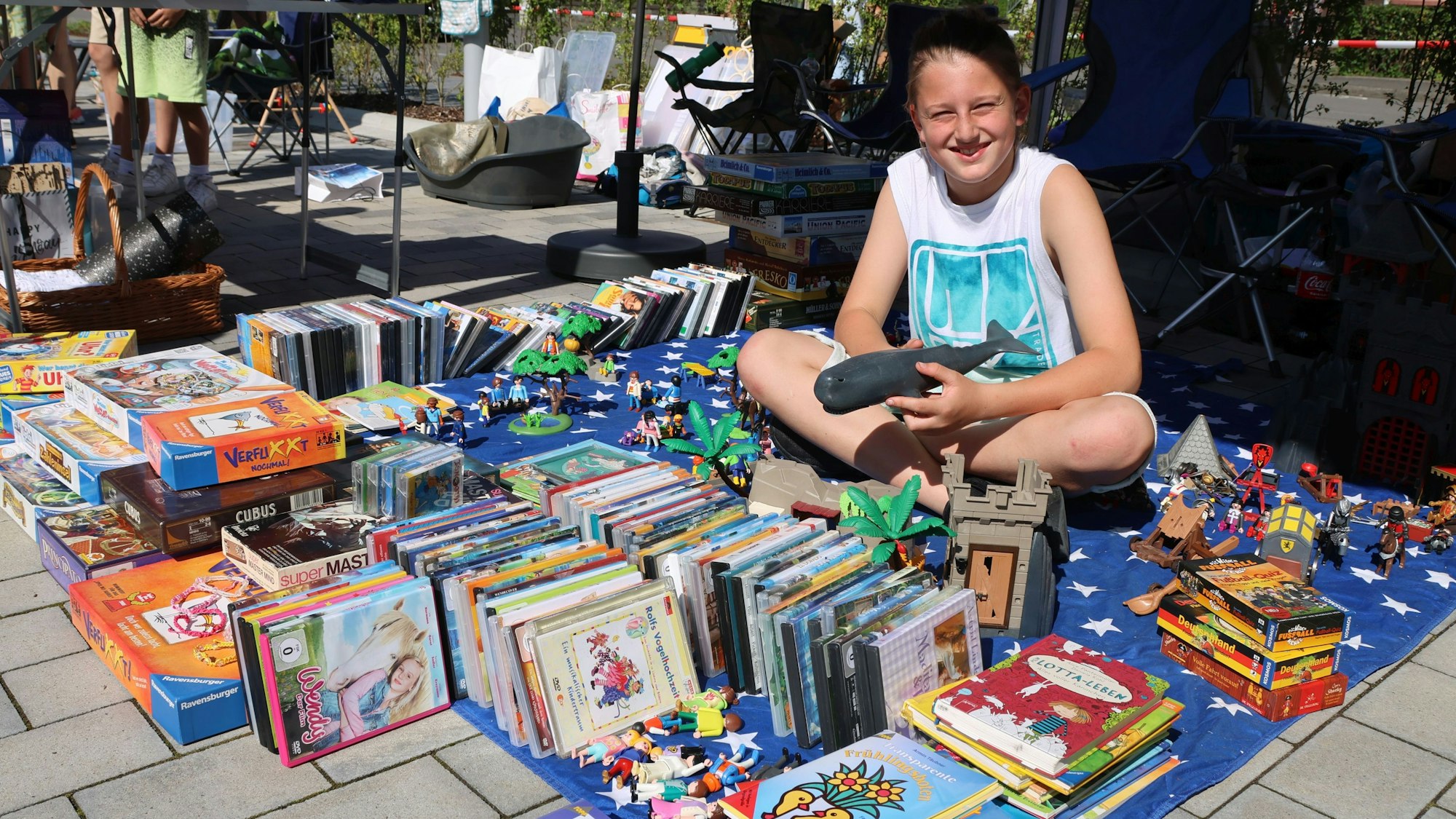 Der Junge Leon Schöffler sitzt auf seiner Verkaufsdecke inmitten vieler Spielsachen und Bücher.