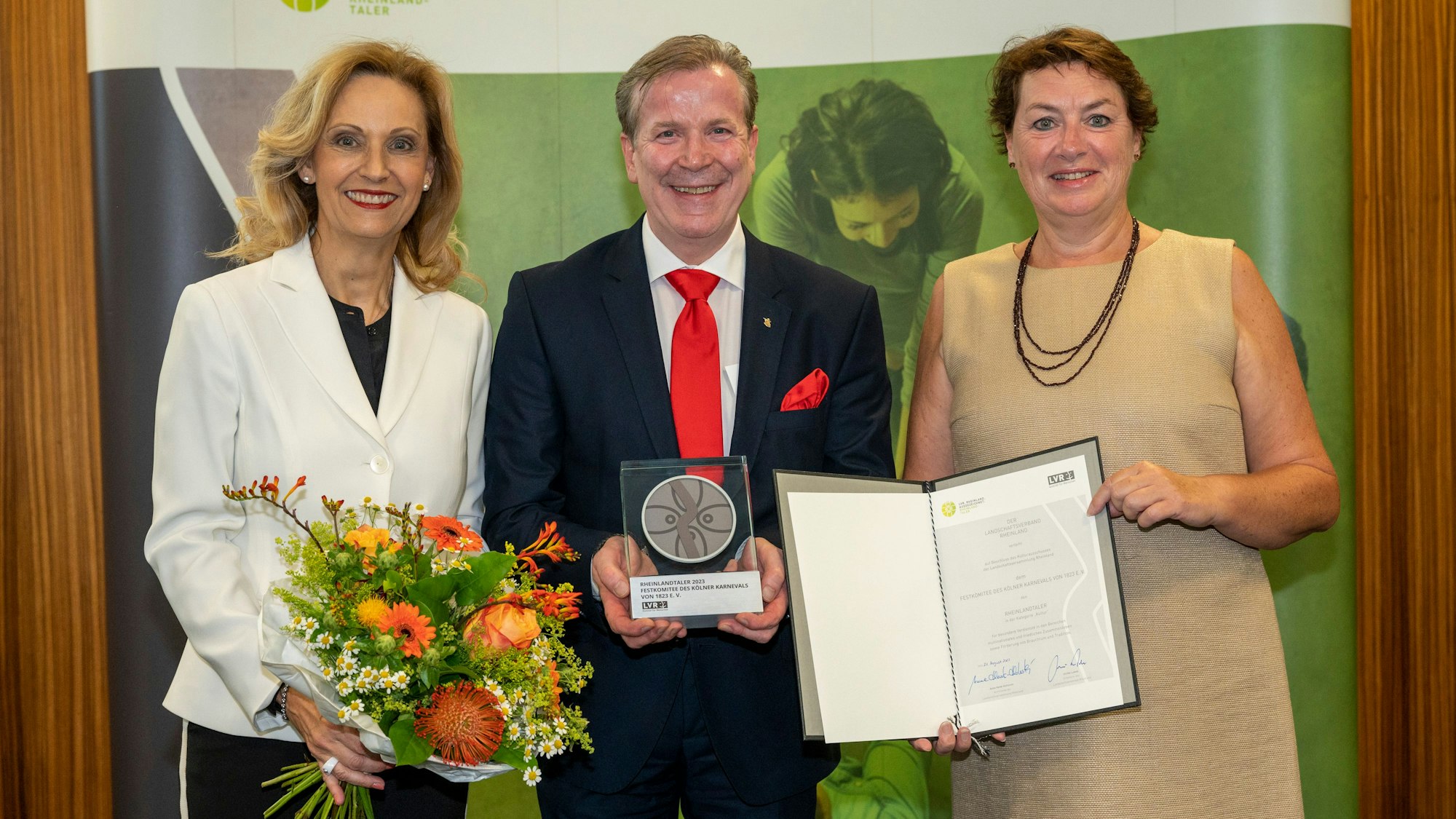 Ulrike Lubek, Christoph Kuckelkorn und Anne Henk-Hollstein (v.l.) stehen lachend nebeneinander. Kuckelkorn hält den Rheinlandtaler.