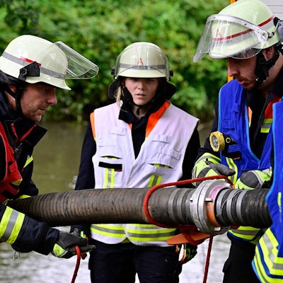 Feuerwehrleutemontieren einen Saugschlauch, um Löschwasser aus einem Fluss im Hintergrund zu fördern.