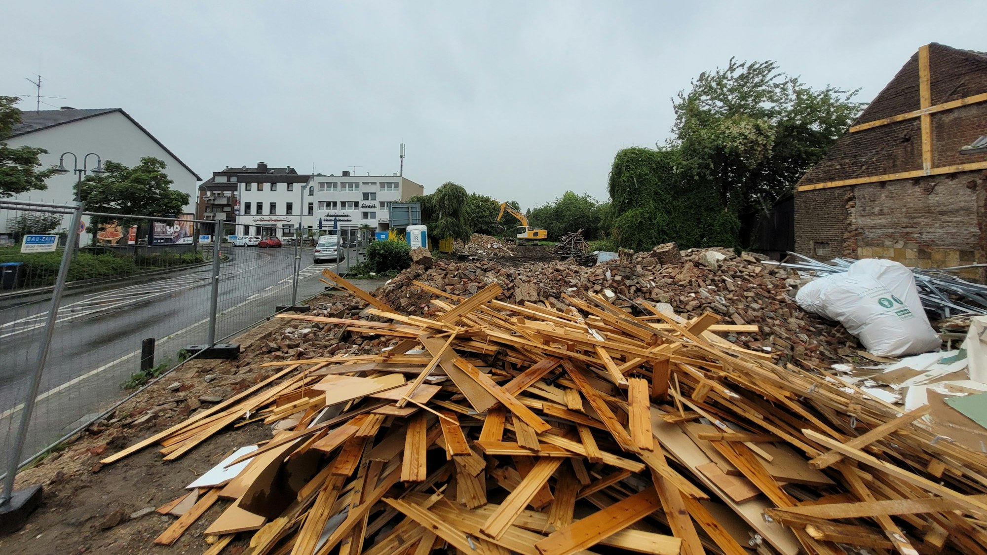 Auf einem Grundstück an einer Straße, das durch einen Bauzaun abgegrenzt ist, liegt Schutt und Holz.