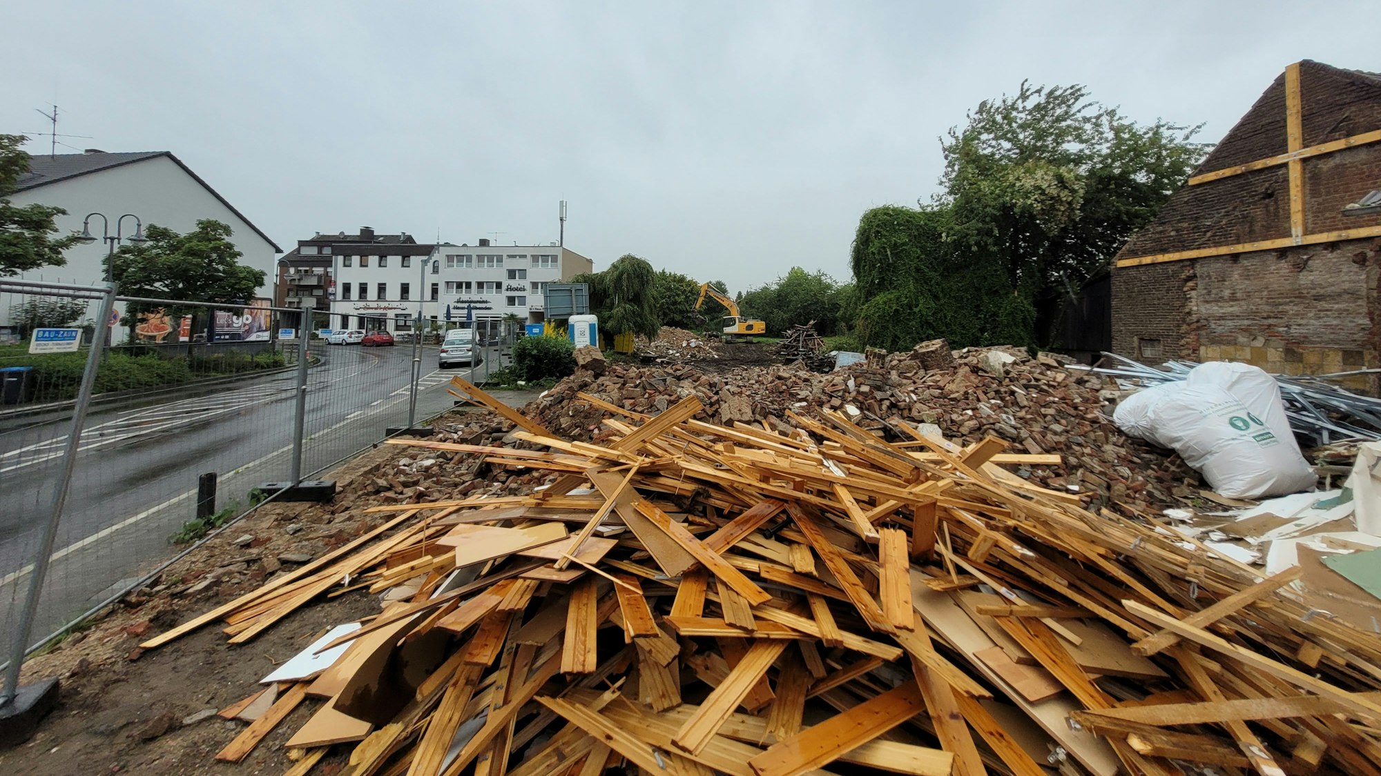 Auf einem Grundstück an einer Straße, das durch einen Bauzaun abgegrenzt ist, liegt Schutt und Holz.