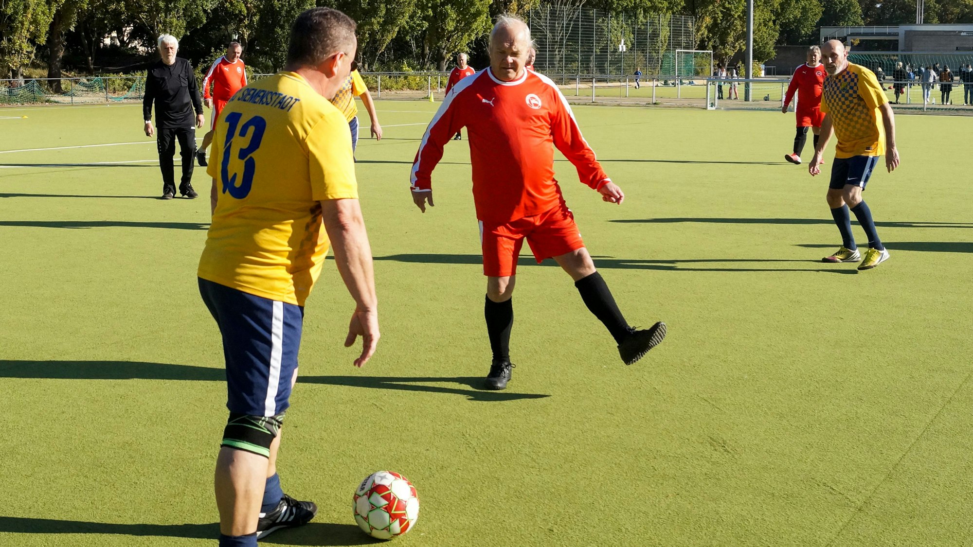 Fußballer in gelben und roten Trikots spielen Walking Football gegeneinander.
