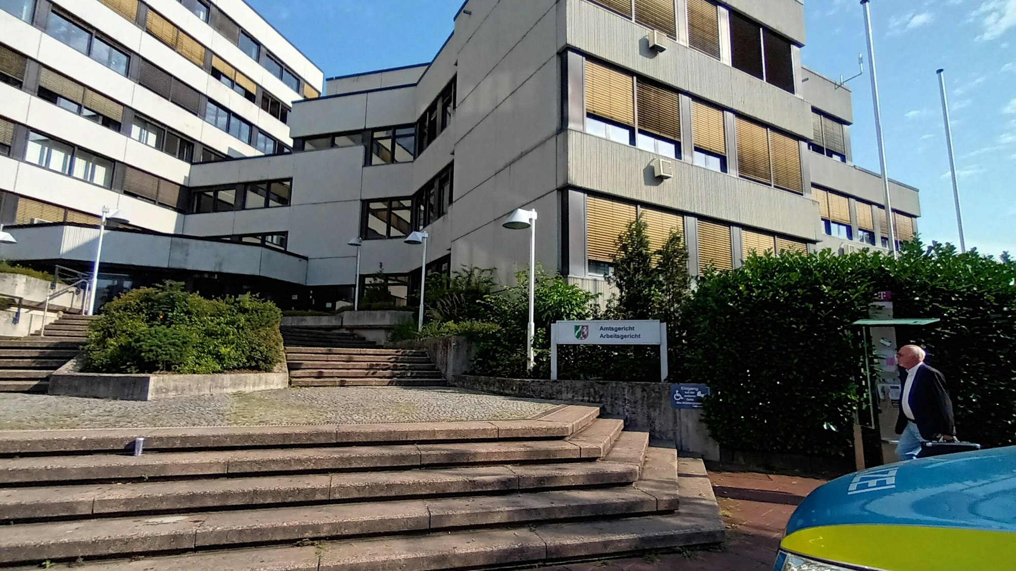 Breite Treppen führen hinauf zu einem weißen, mehrstöckigen Gebäude mit Fensterreihen.