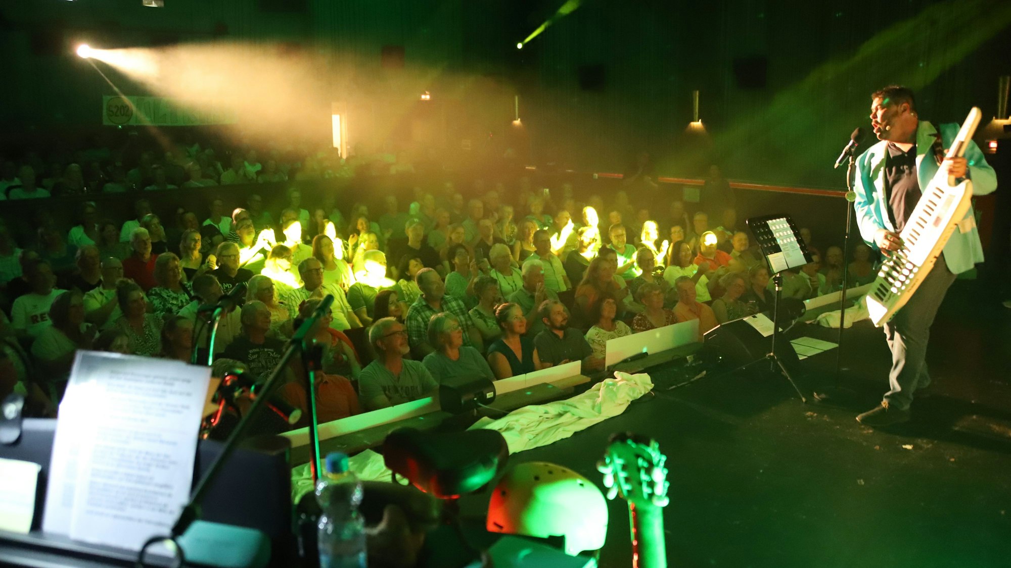 Blick von der Bühne, auf der Uli Birkmann mit einem Umhänge-Keyboard eine Persiflage auf den Italo-Pop spielt, ins voll besetzte Publikum.