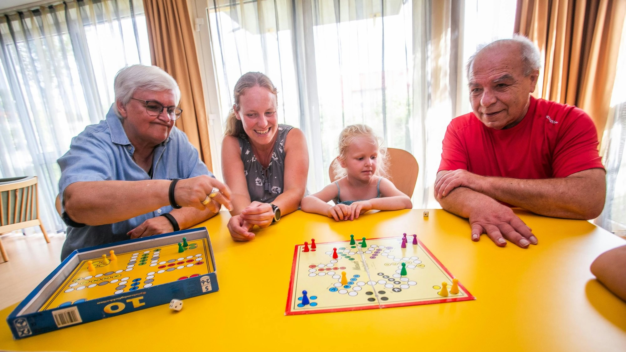 Angelika Floßbach, Tanja Lang, Zoe und Bernd Hönkhaus sitzen an einem Tisch im CBT-Mehrgenerationenwohnhaus in Wipperfürth und spielen Mensch-Ärgere-Dich-Nicht.