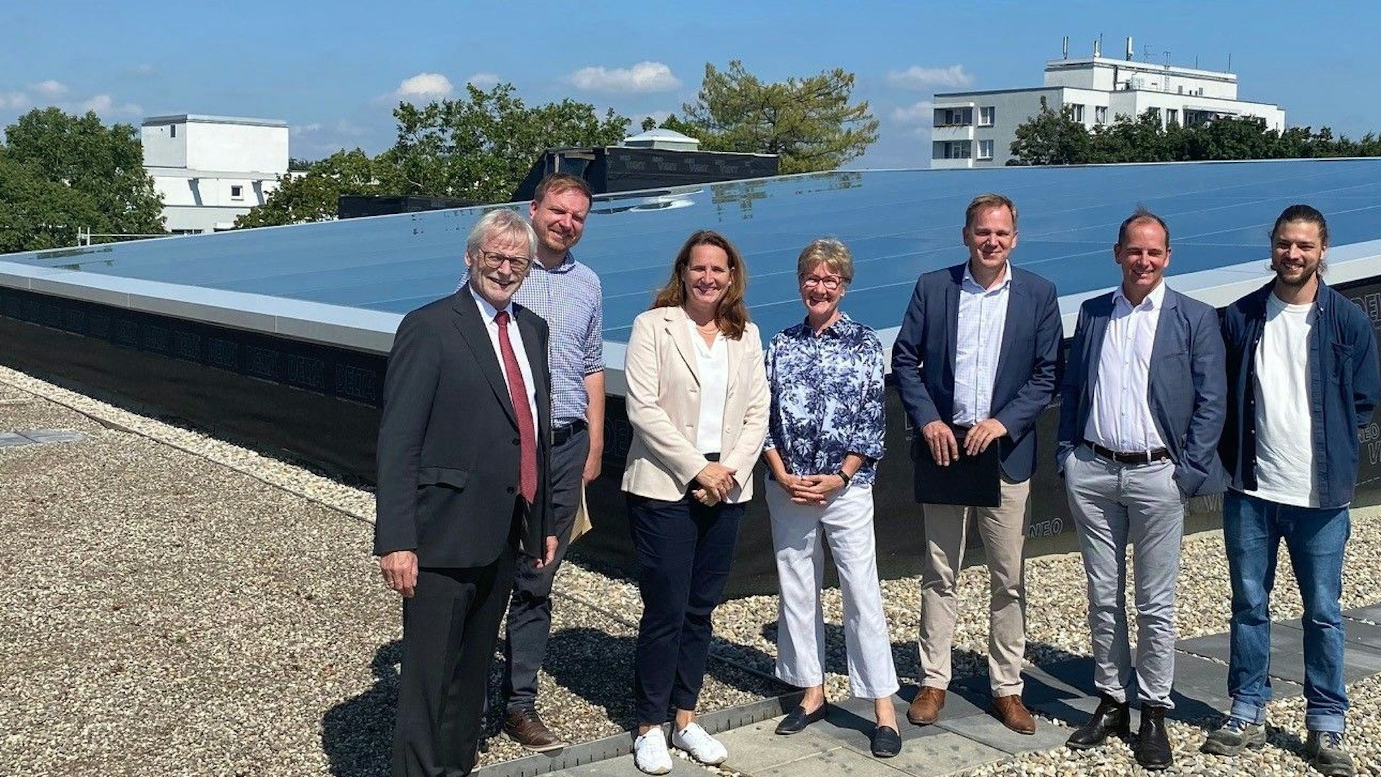 Auf dem Dach, vor dem großen Glaselement stehen die zufrieden aussehenden Verantwortlichen.