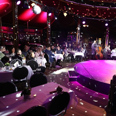 Ein Künstler steht auf der Bühne im Altenberger Spiegelzelt. Menschen sitzen an Tischen bei der Dinnershow mit dem Kölner Cirque Bouffon.
