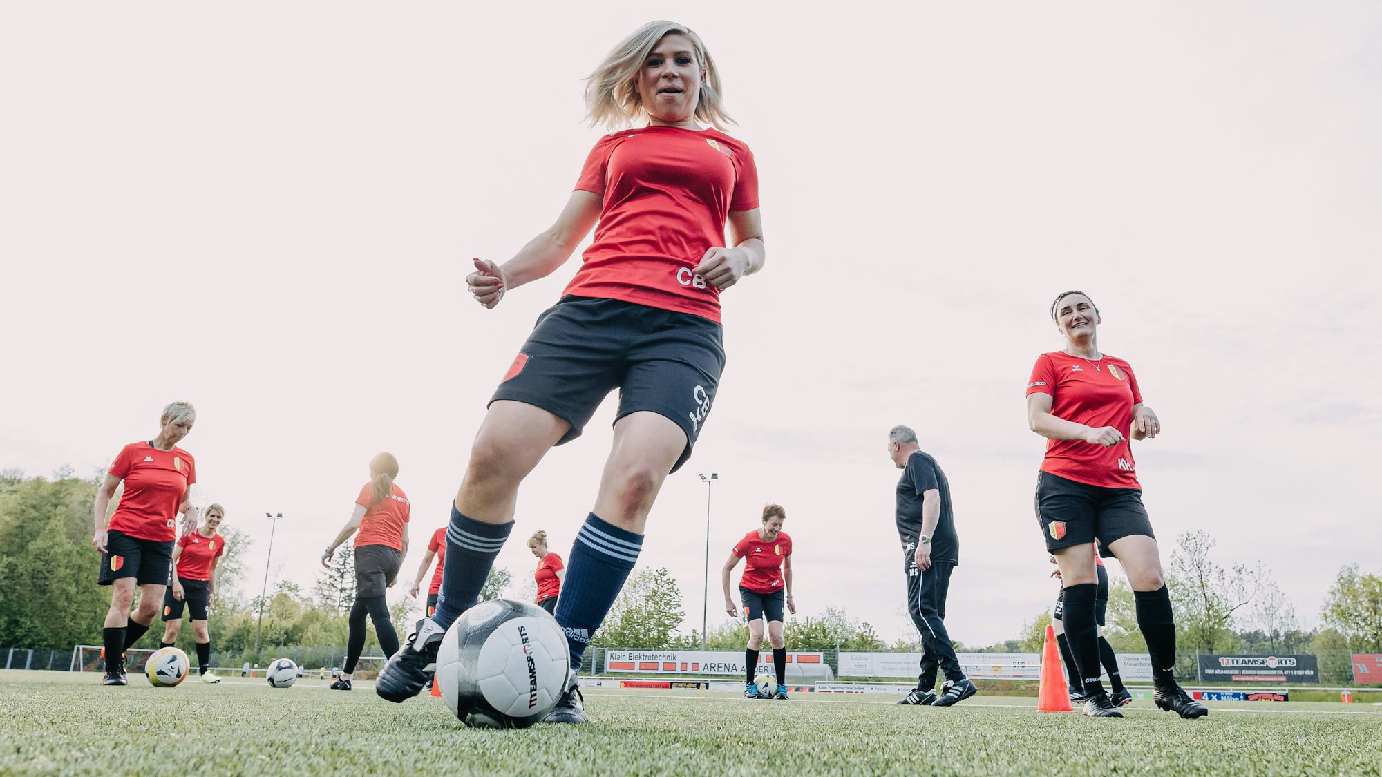 Eine Fußballerin dribbelt den Ball an der Kamera vorbei. Hinter ihr trainieren ihre Mannschaftskameradinnen in roten Trikots.