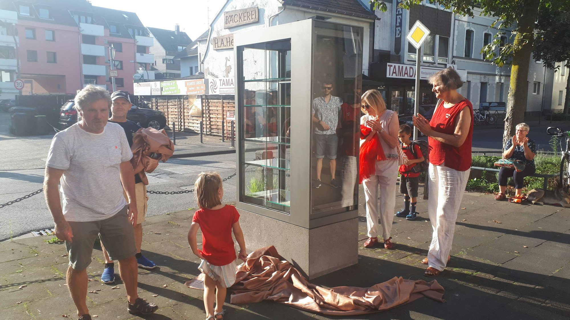 Auf dem Bürgersteig an einer kleinen Straße steht ein nagelneuer Schrank mit Glasscheiben und Glasböden für Bücher.