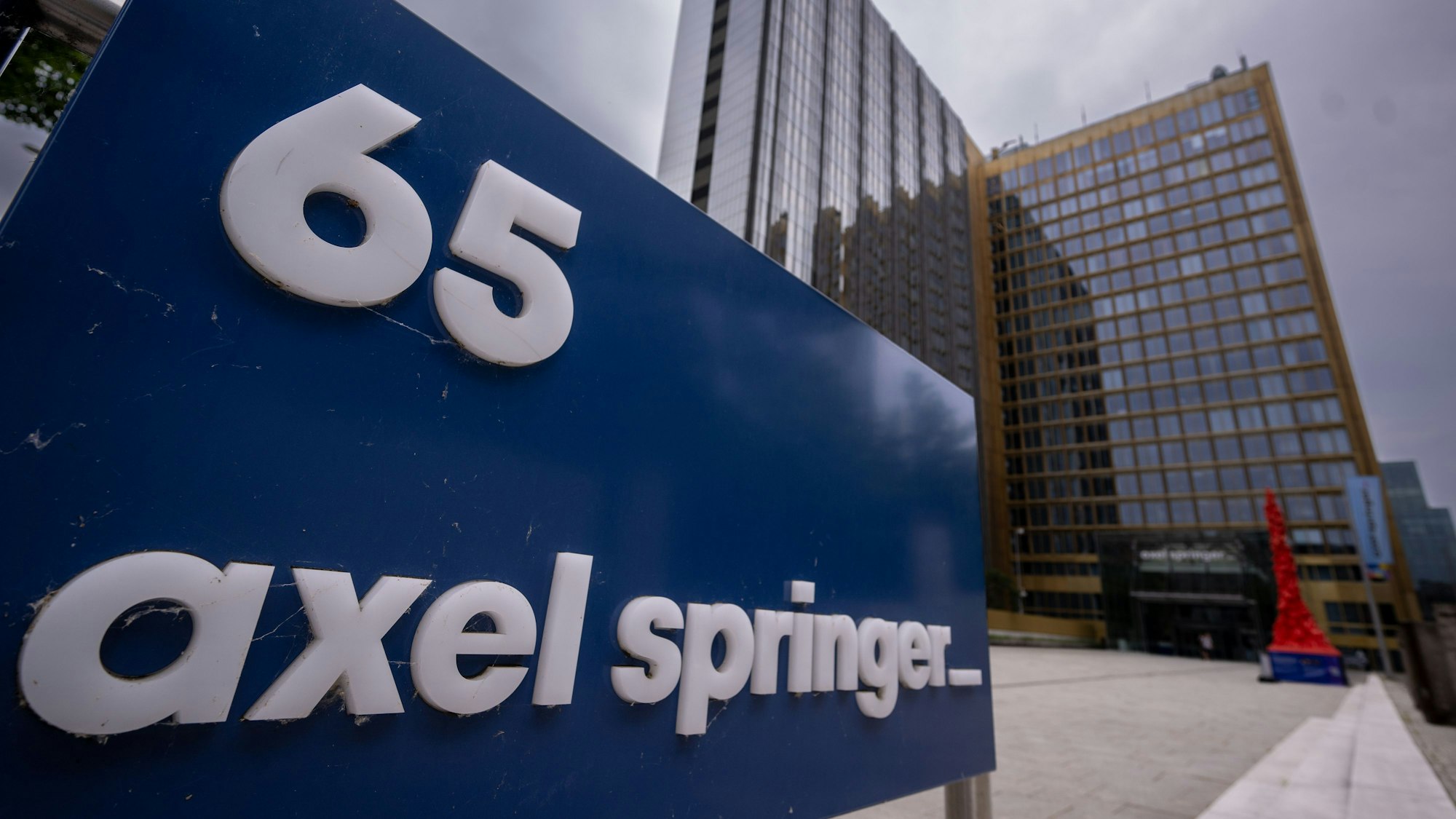 Eine Tafel mit dem Logo vom Axel-Springer-Verlag und der Hausnummer 65 steht vor dem Verlagsgebäude. Der Medienkonzern Axel Springer hat sich mit dem ehemaligen Angestellten Julian Reichelt außergerichtlich geeinigt. (Symbolbild)