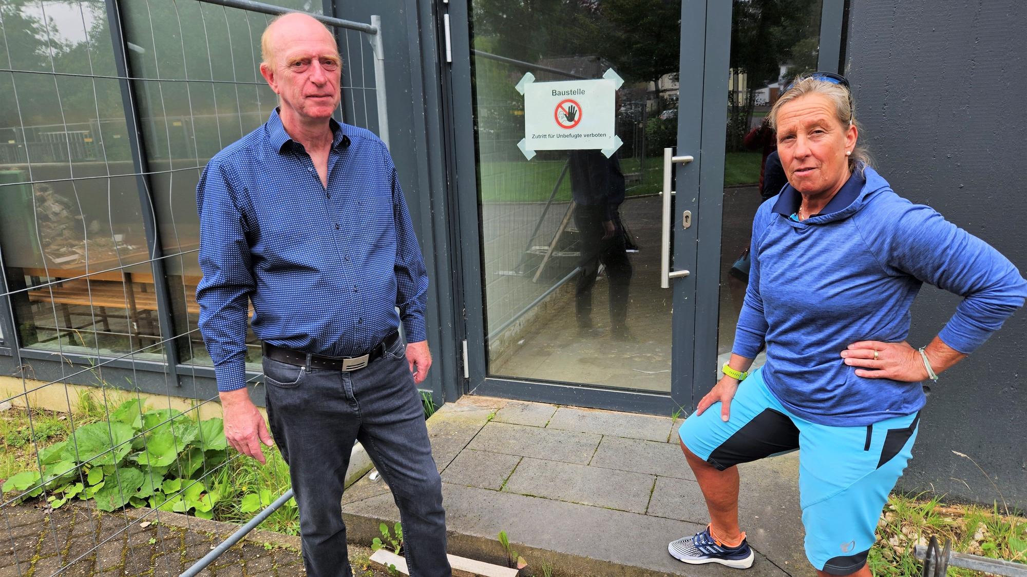 Vor dem Eingang der Halle stehen Richard Fremery und Iris Schröder vom TV Kall. An der Eingangstür hängt ein Warnschild mit der Aufschrift „Baustelle“. Neben der Tür: ein Bauzaun.