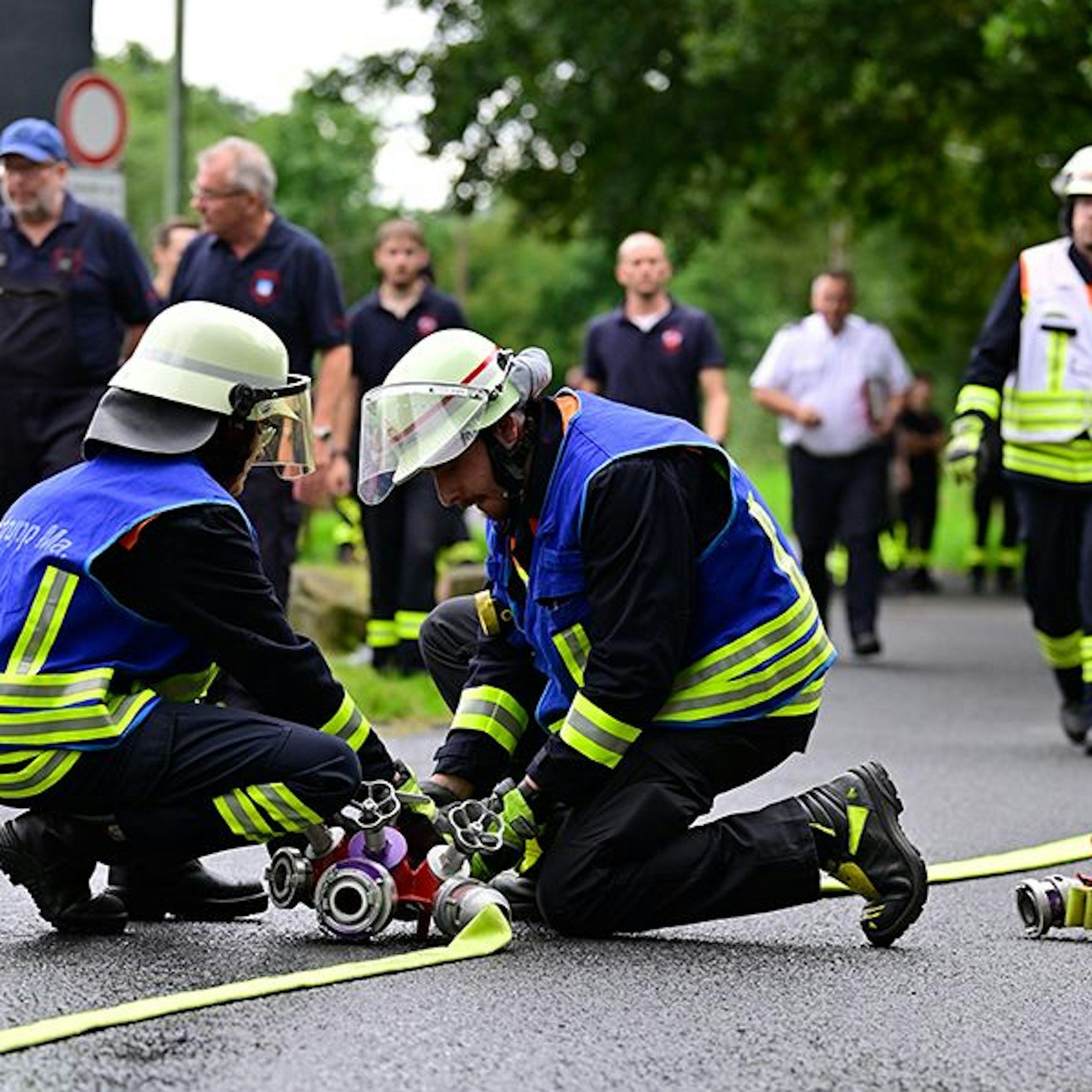 Feuerwehrleute montieren einen Wasserverteiler auf einer Straße.