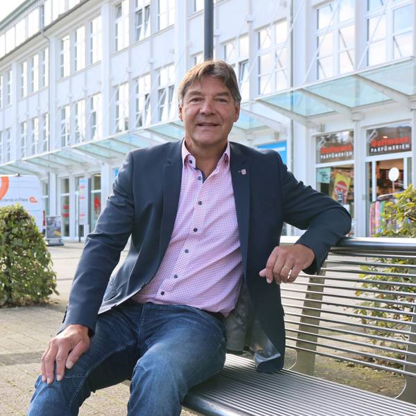 Zu sehen ist ein Mann, der vor dem Rathaus in Bergneustadt auf einer Bank sitzt.