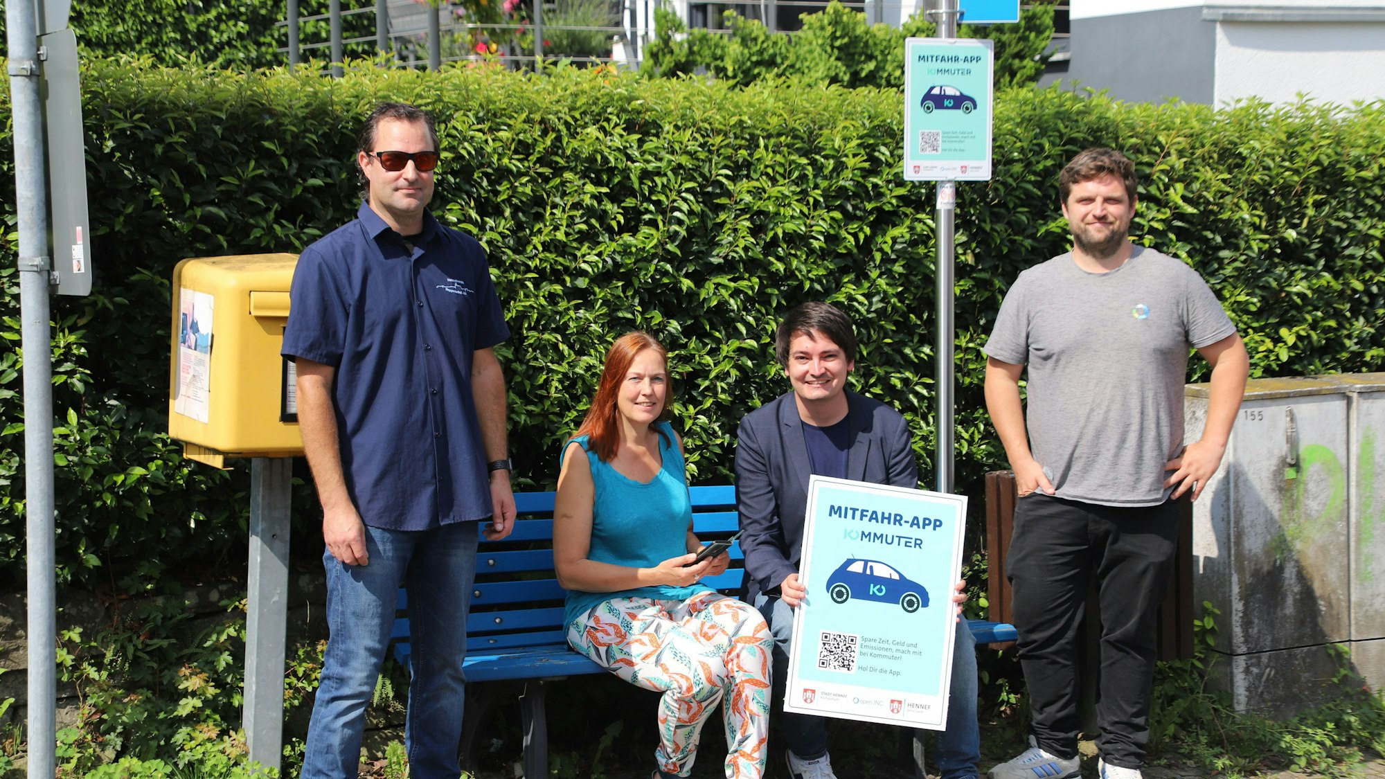 Die Stadt Hennef bietet jetzt die Mitfahrapp Kommuter an, die Mitfahrbänke sind darin enigebunden. An der Mitfahrbank Hennef trafen sich (v.l.): Jens Nowak, Vorsitzender Heimatverein Happerschoß, Klimaschutzmanagerin Annette Flintemann, Bürgermeister Mario Dahm und Martin Stein, Entwickler der App von OpenInc.