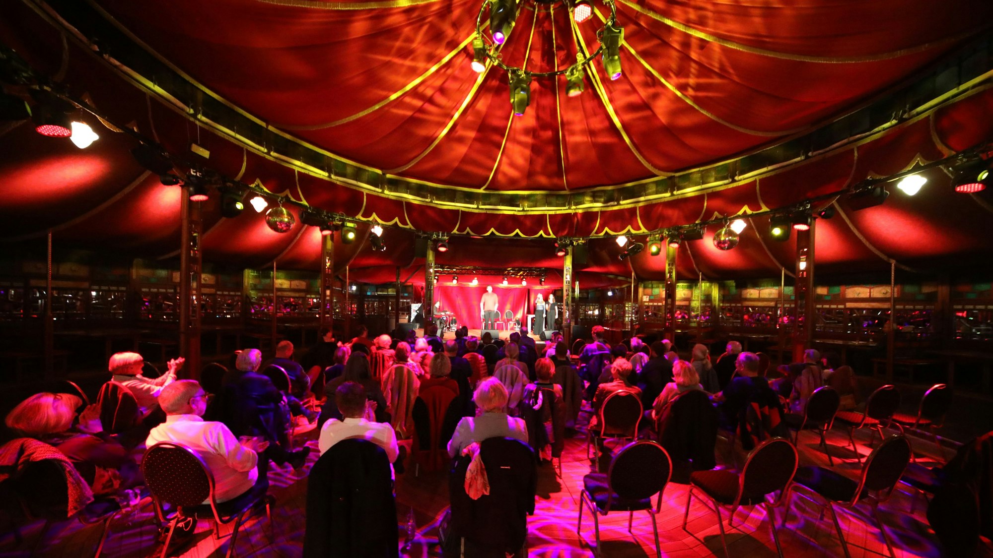 Menschen sitzen auf Stühlen unter einem roten Spiegelzelt-Dach.