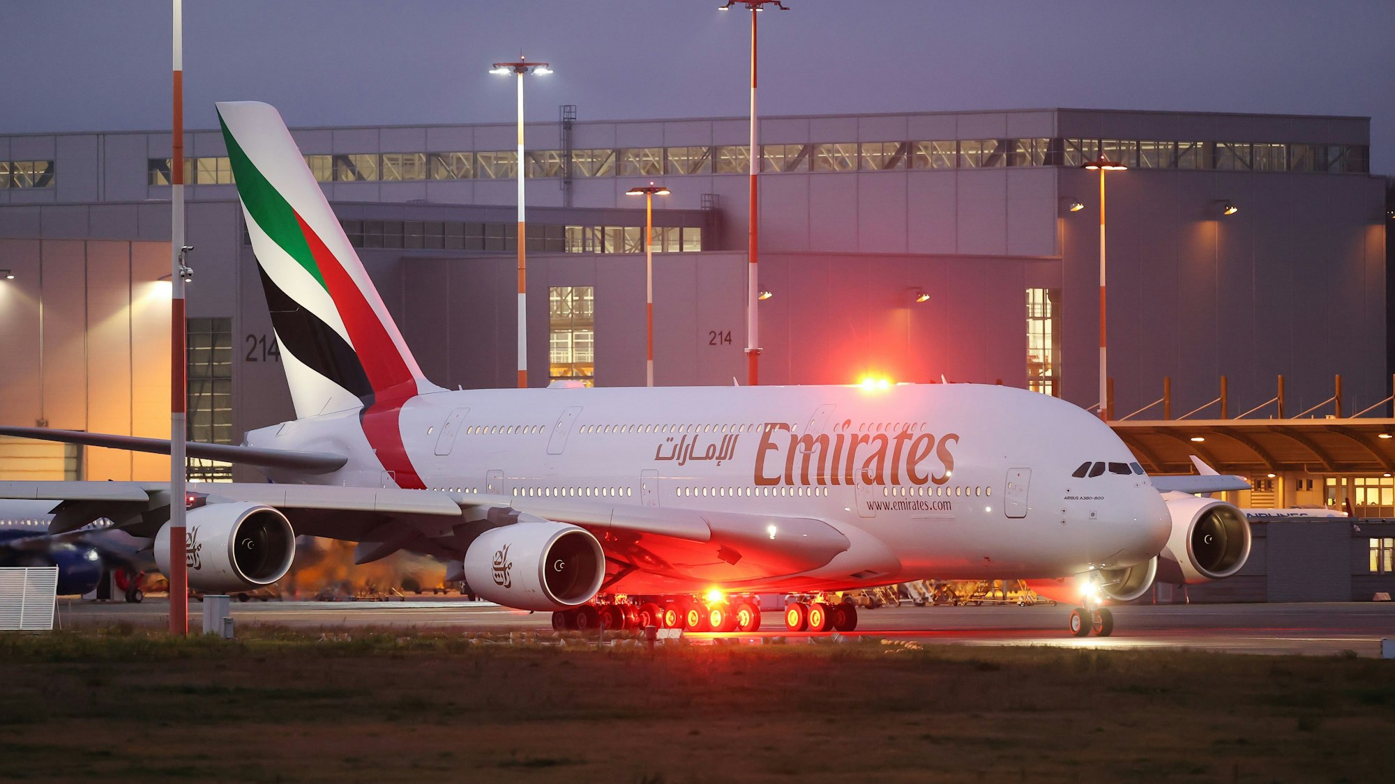 Ein Airbus A380 der arabischen Fluggesellschaft Emirates steht vor roten Warnlichtern vor einem Flughafengebäude.
