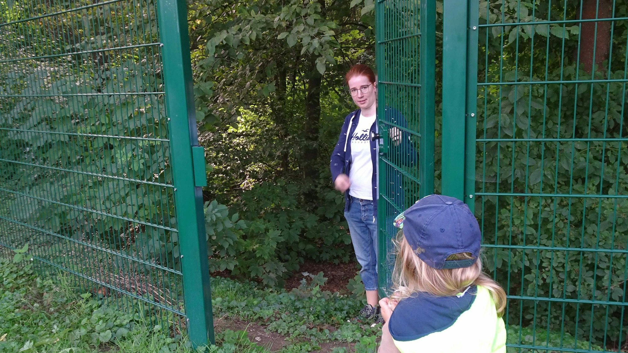Erzieherin Svenja Umlauf öffnet das grüne Tor, durch das die Kinder bisher noch nicht gegangen sind. Der Trampelpfad dahinter führt vom eingezäunten Gelände des Bauwagens in den Wald.