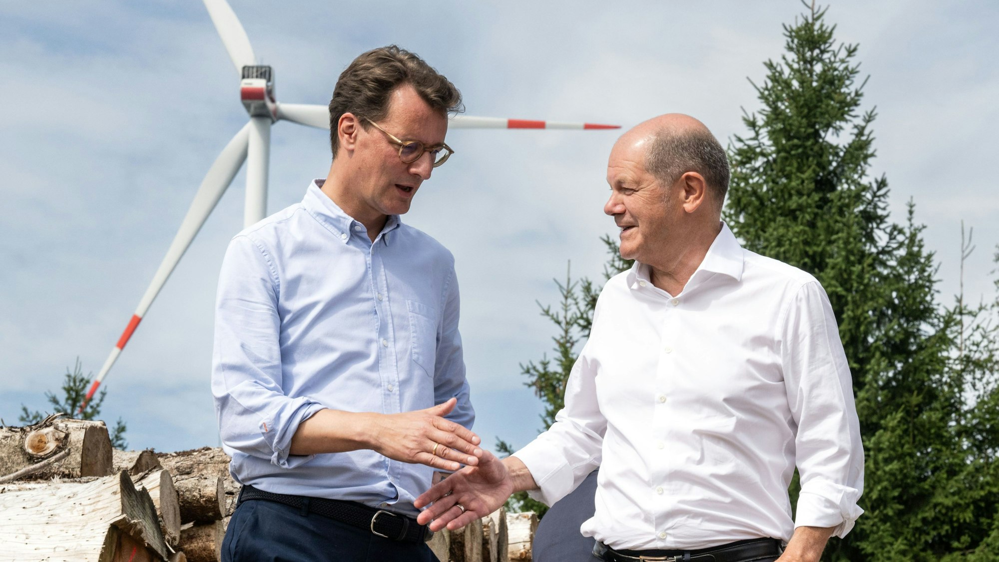 Bundeskanzler Olaf Scholz und Hendrik Wüst reichen sich die Hand. Im Hintergrund ist ein Windrad.