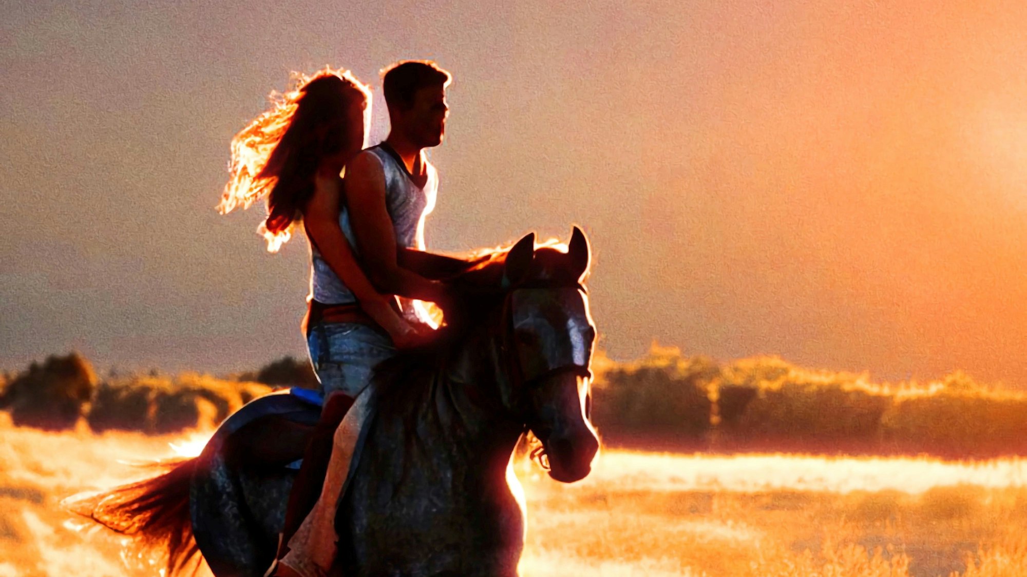 Ein Mann sitzt mit einer Frau auf dem Rücken eines Pferdes im Sonnenuntergang.