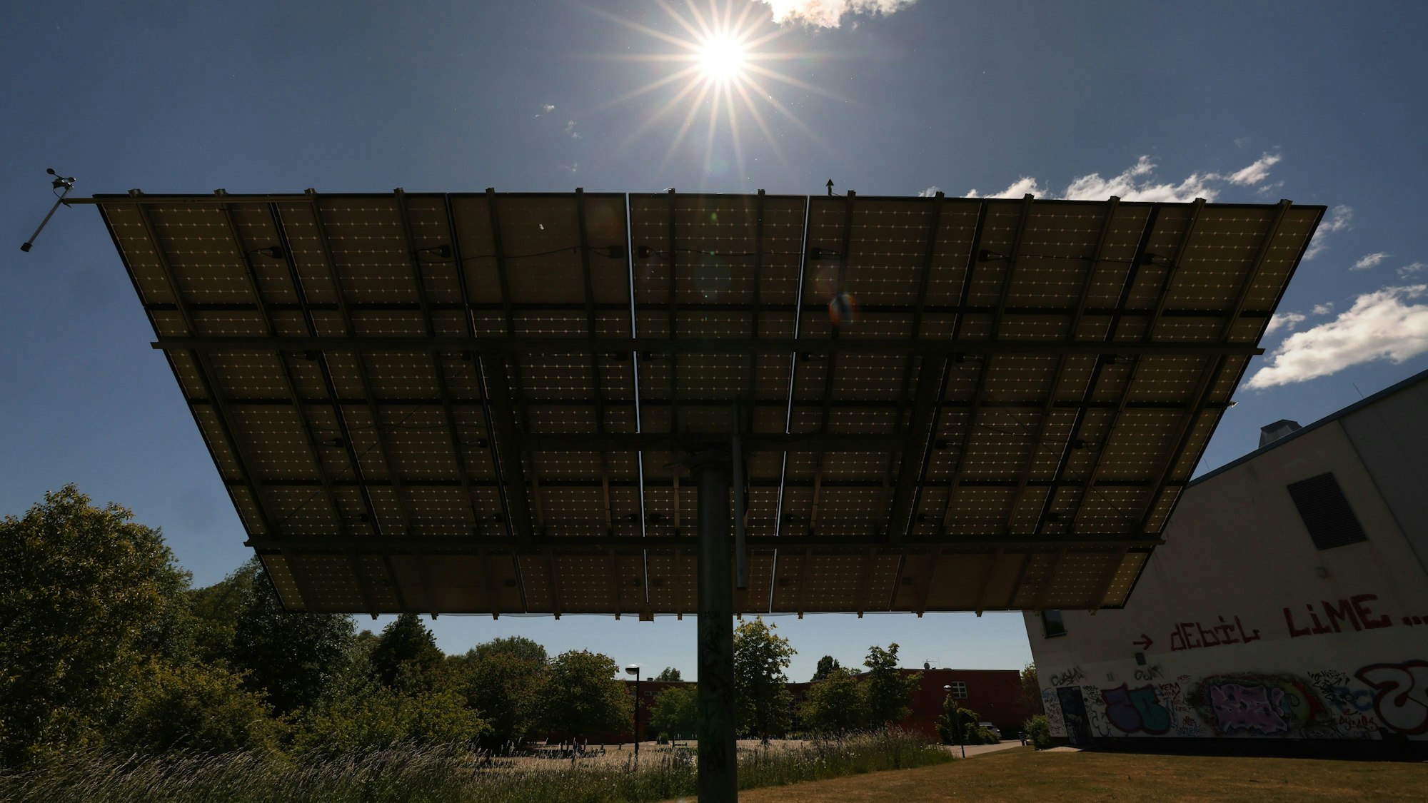 Auf einer Wiese neben einer Sporthalle stehen Solaranlagen auf einem Ständer, auf dem sie dem Sonnenlicht nachgeführt werden können.