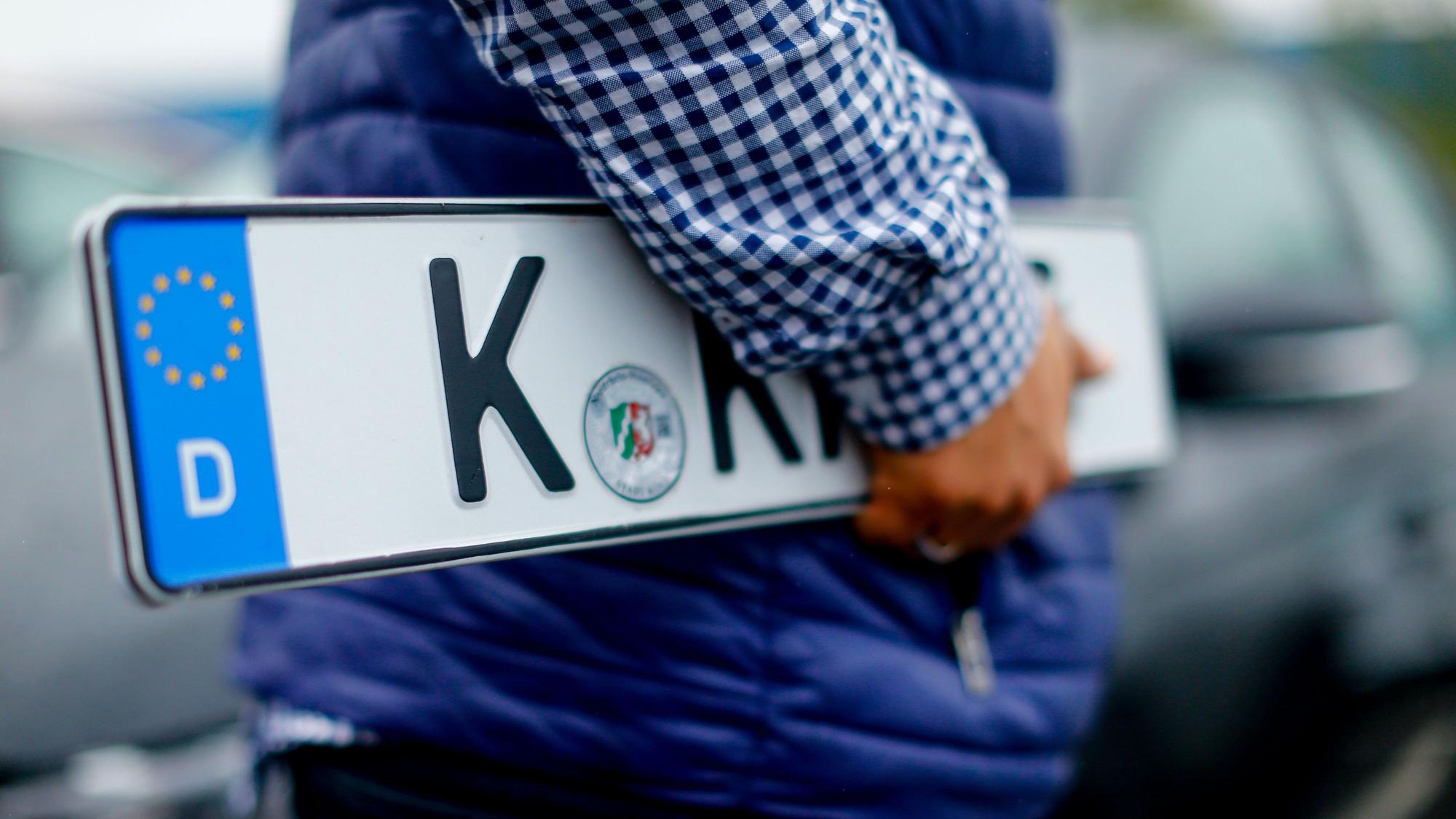 Ein Kunde trägt Nummernschilder vor der KFZ-Zulassungsstelle in Köln-Poll