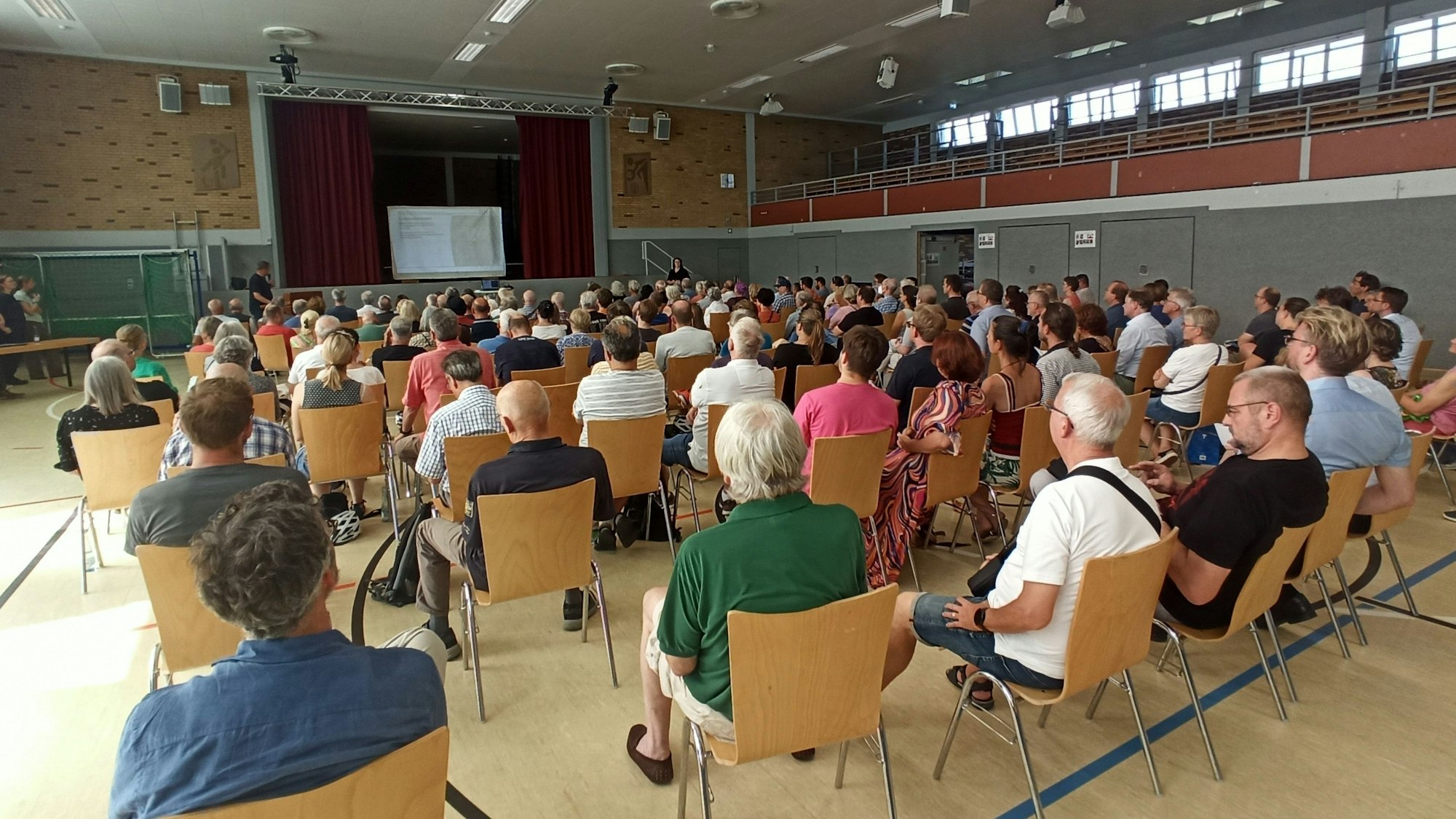 In einer Halle sitzen viele Personen auf Stühle.