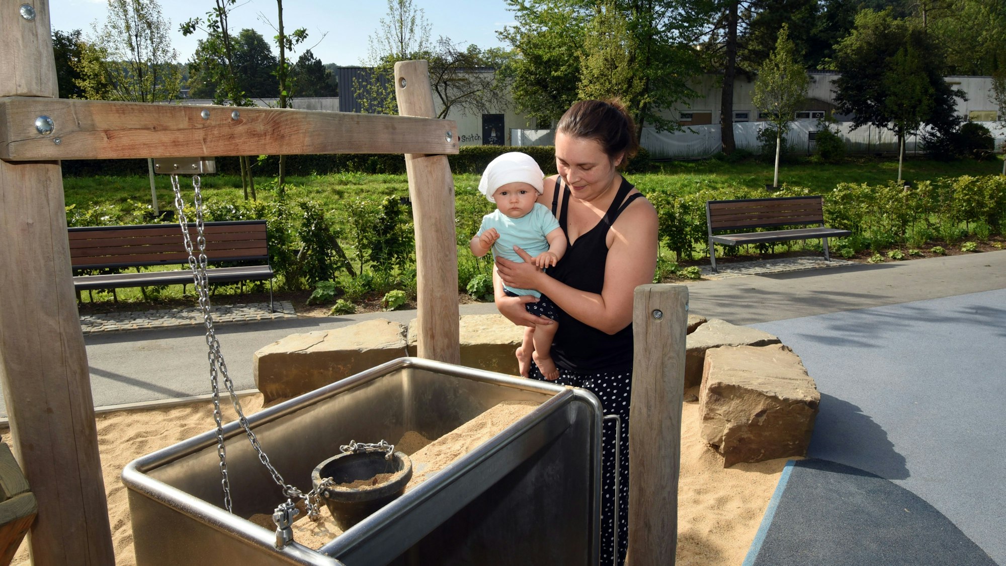 Eine junge Mutter und ihr Kleinkind stehen an einem Sandspielgerät.