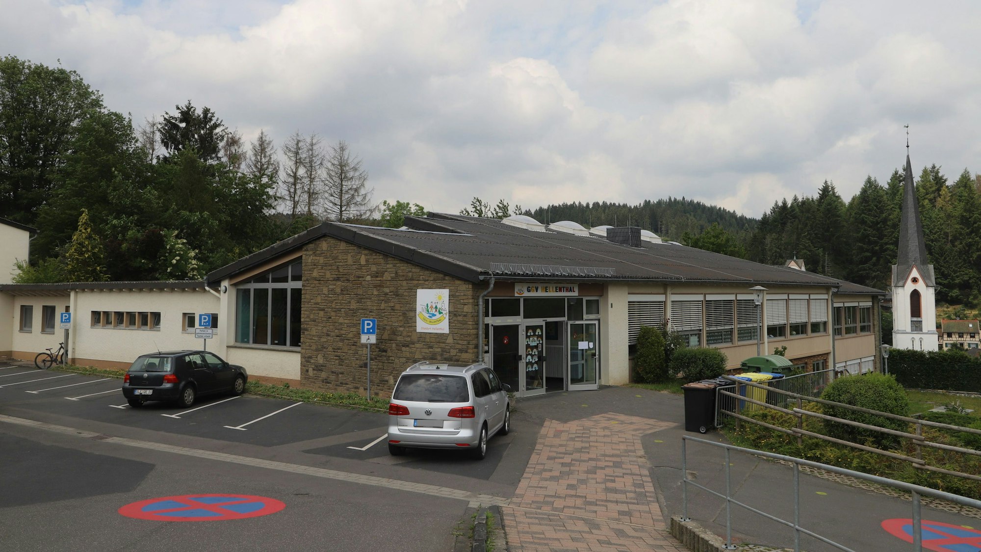 Auf dem Bild ist die Grundschule Hellenthal von außen zu sehen, im Hintergrund der Turm der Kirche.