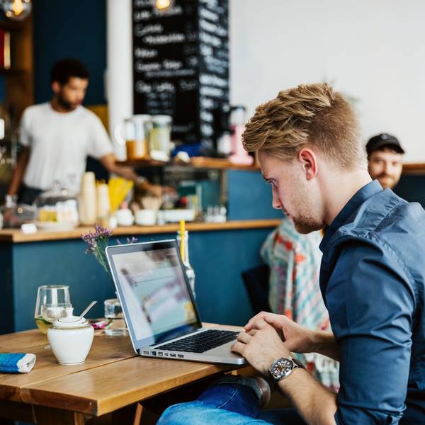 Ein junger Mann arbeitet in einem Café an seinem Laptop.