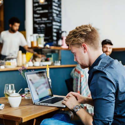 Ein junger Mann arbeitet in einem Café an seinem Laptop.