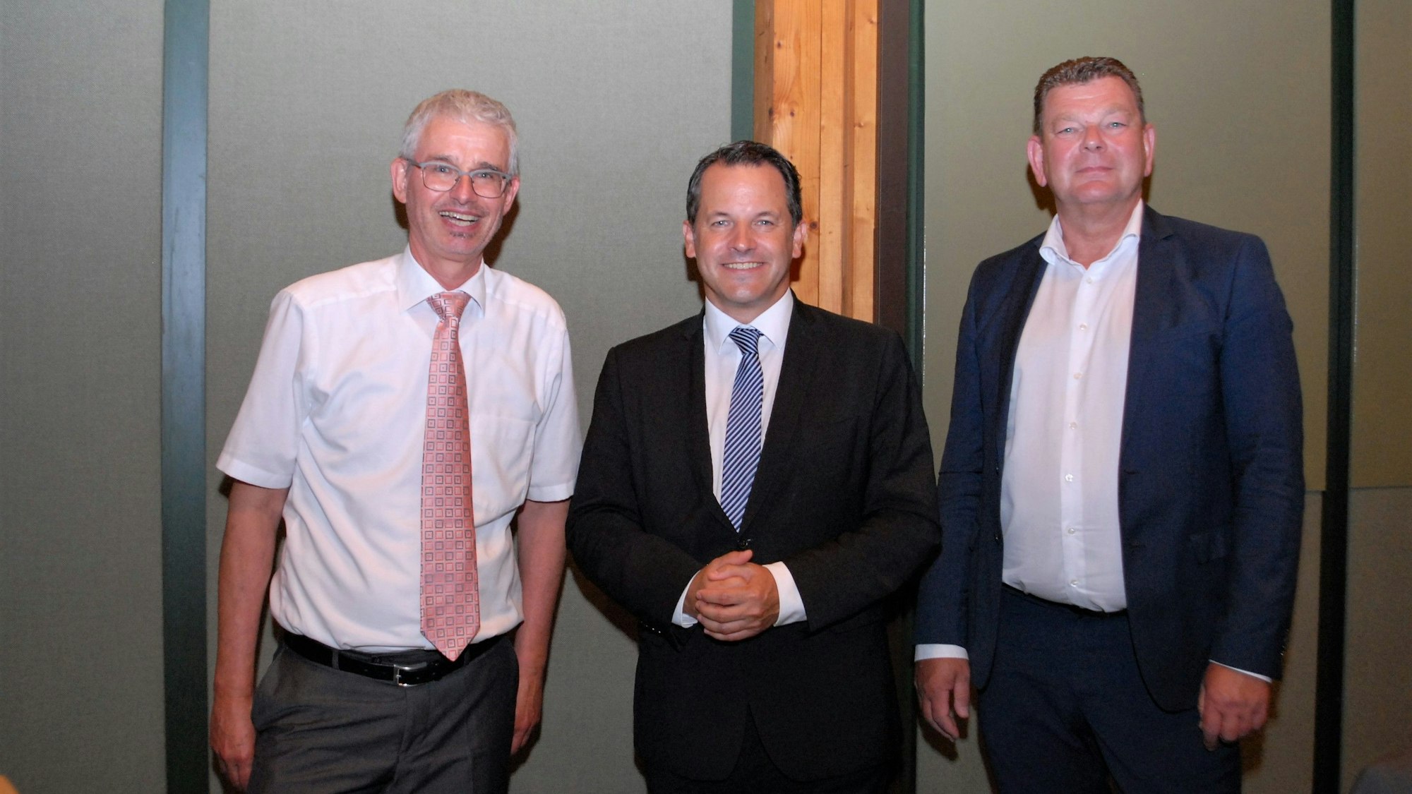 Drei Männer sind teilweise in Anzügen und Krawatten gekleidet.