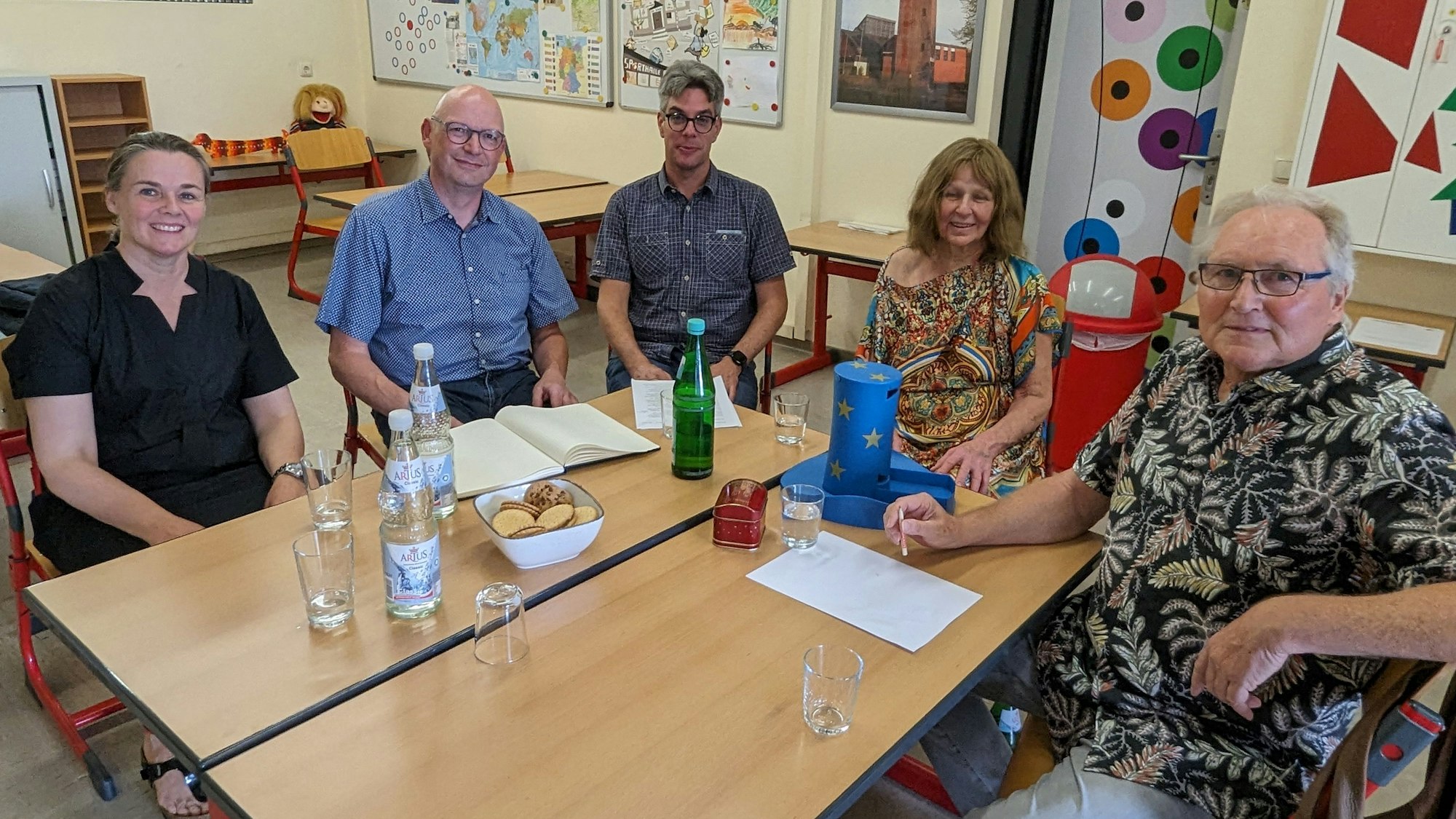 Fünf Männer und zwei Frauen sitzen um zwei zusammengestellte Schultische herum.