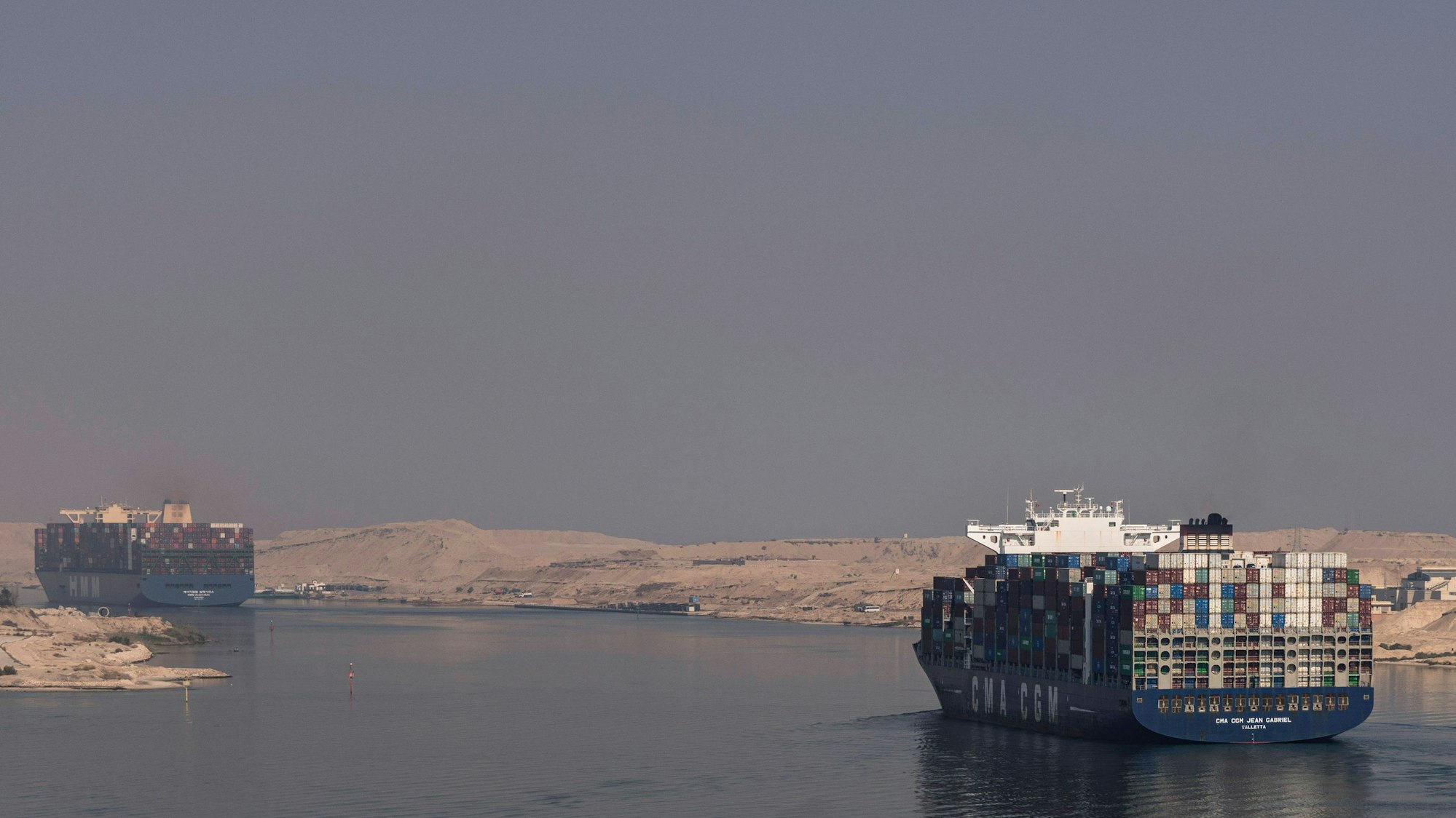 Zwei Frachtschiffe fahren durch den Suezkanal in Ägypten. Links und rechts vom Ufer ist Wüste zu sehen. (Symbolbild)