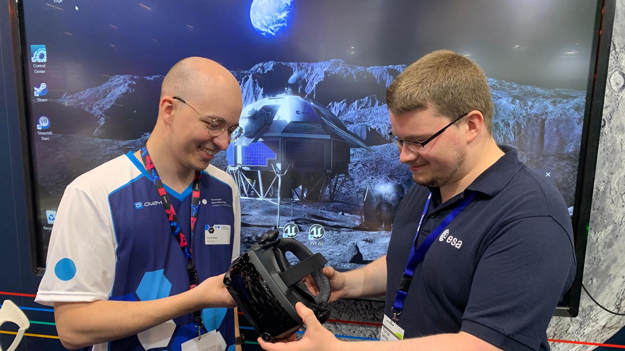Student David Reiter steht vor einer Simulation der Mondoberfläche. Er unterhält sich mit Florian Salzig, der bei der Hochschule Bonn-Rhein-Sieg studiert und nach seinem Masterabschluss zum DLR gegangen ist.