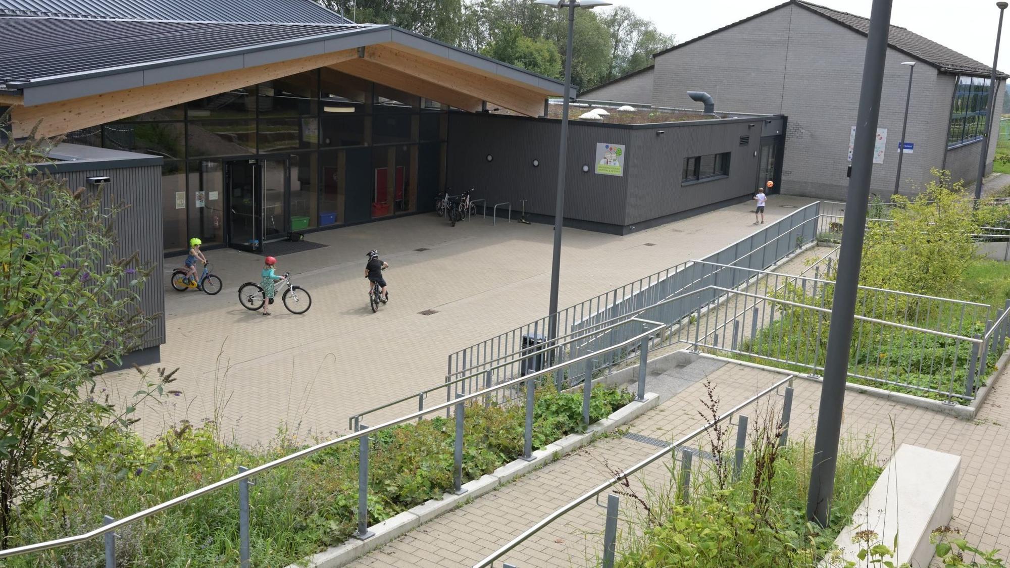 Ein modernes Schulgebäude,davor fahren drei Kinder Fahrrad.