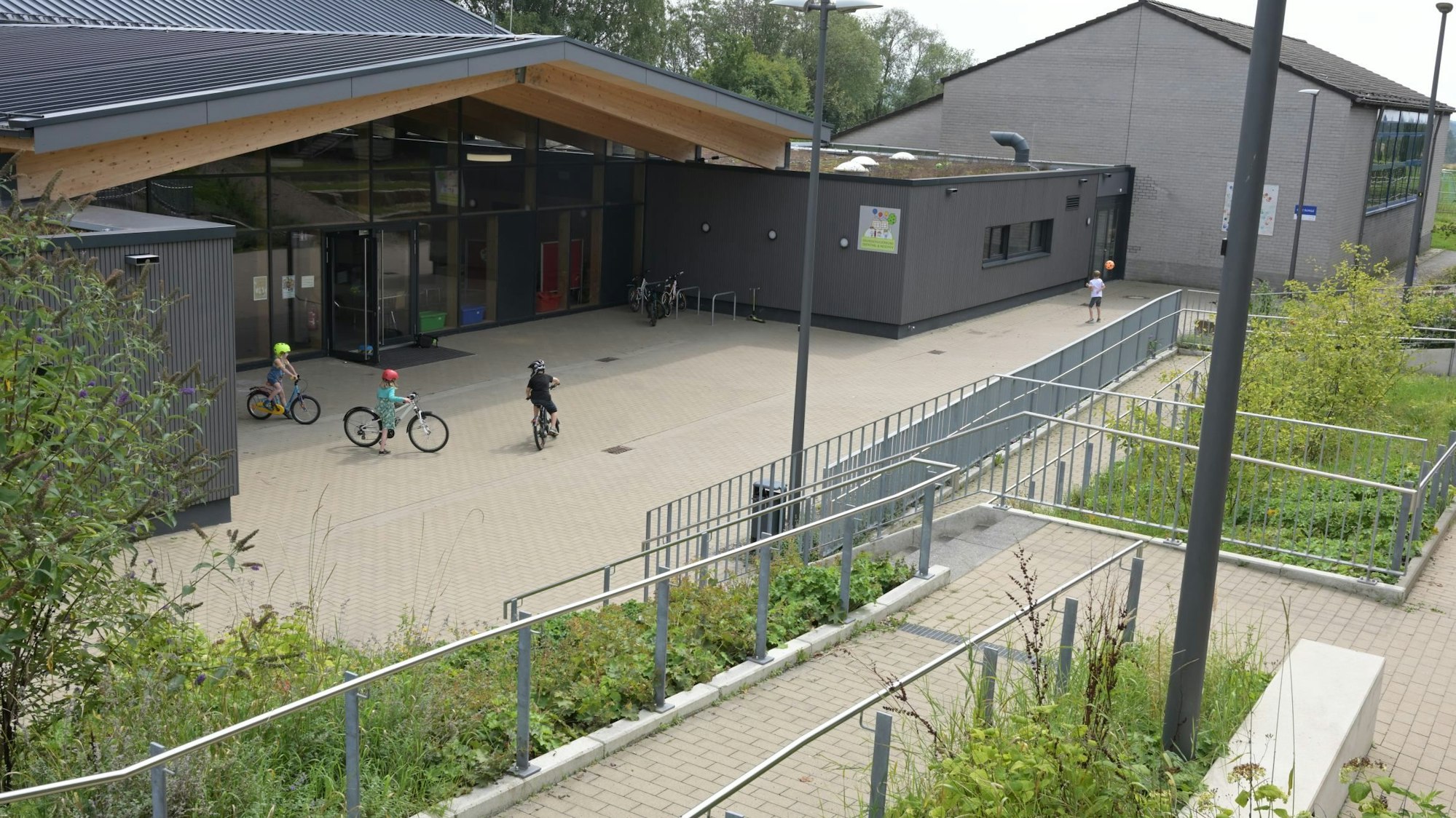 Ein modernes Schulgebäude,davor fahren drei Kinder Fahrrad.